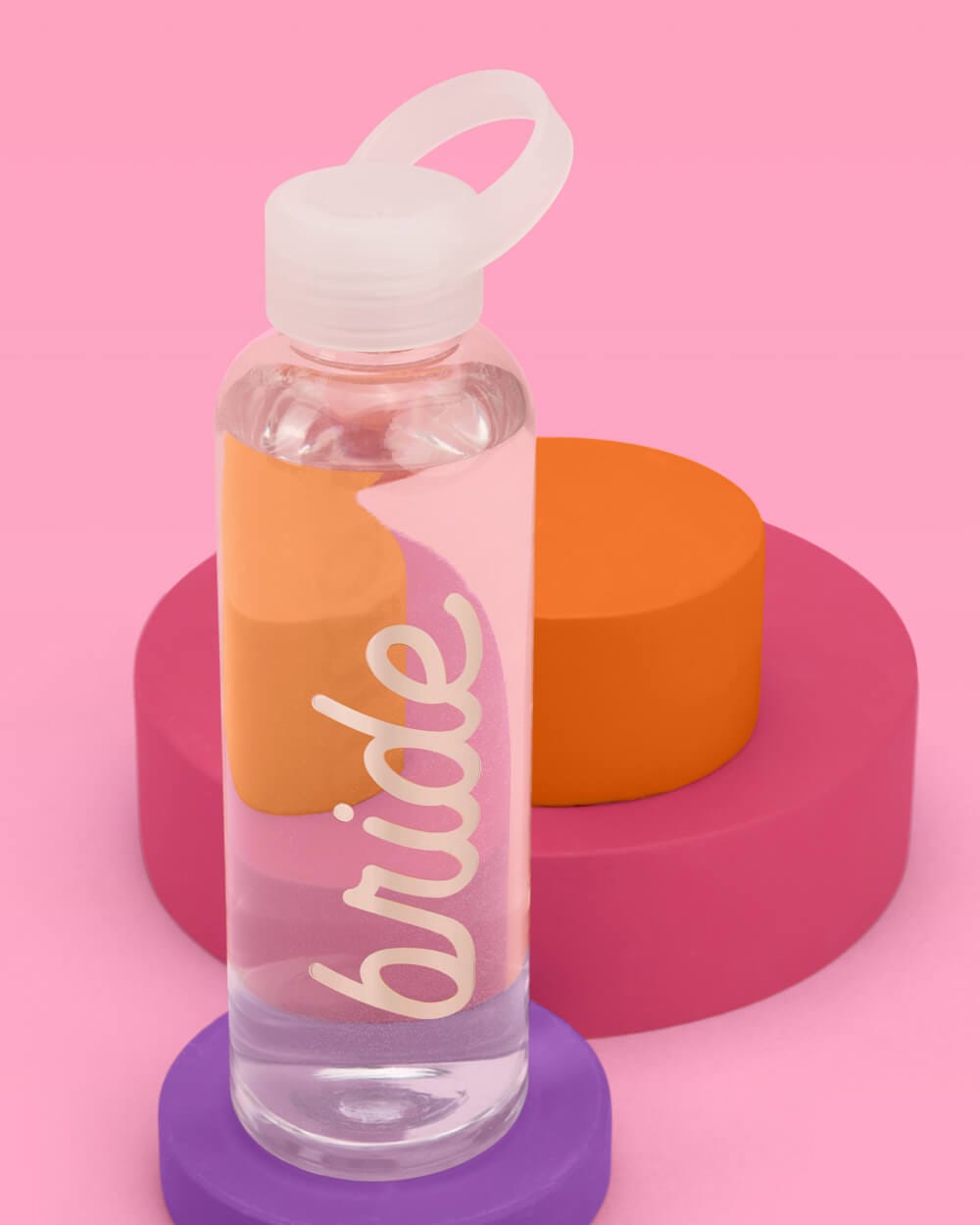 Clear water bottle with white flip-top cap and "bride" text in white script, displayed on colorful stacked rings against pink background.