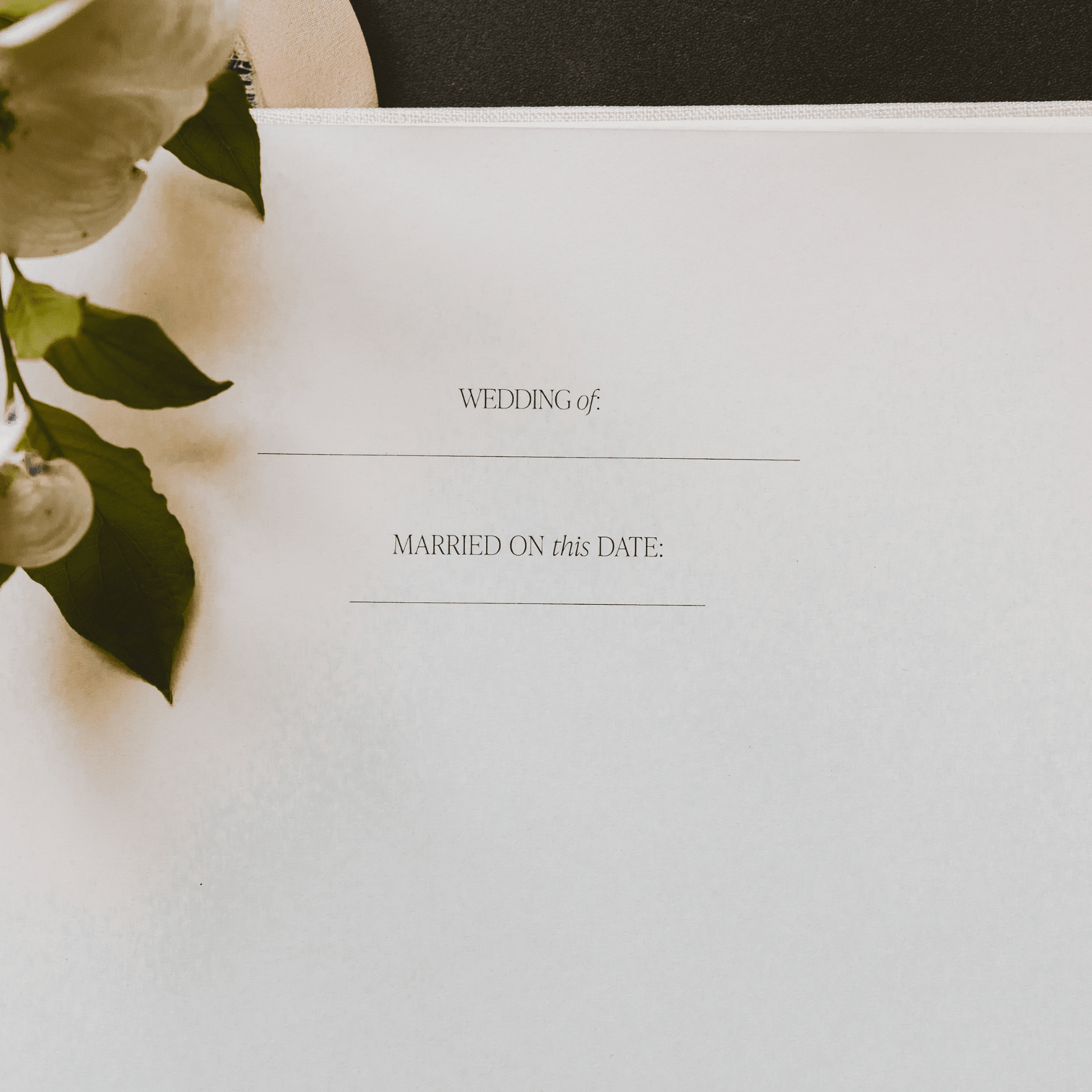 Tan wedding guestbook with "Wedding of" and "Married on this date" text, styled with white roses and greenery.