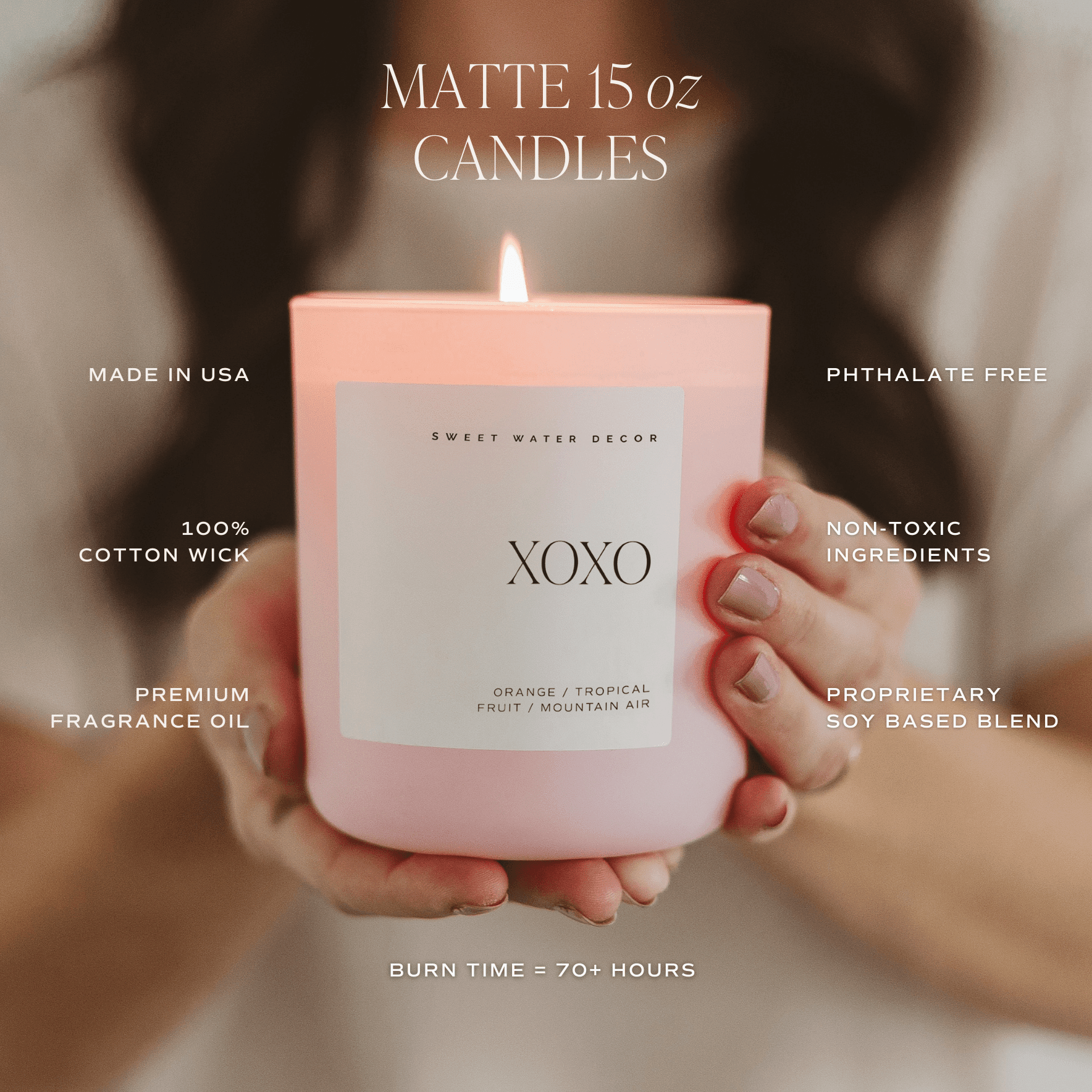 Pink matte 15 oz soy candle labeled XOXO held in hands with lit flame visible
