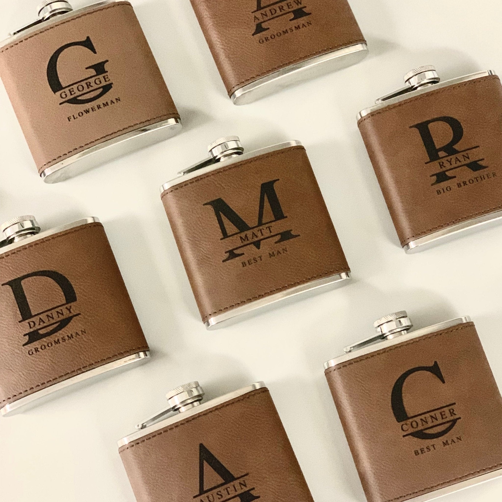 Tan leather flasks with monogram letters and decorative lines, arranged on white background with metal caps