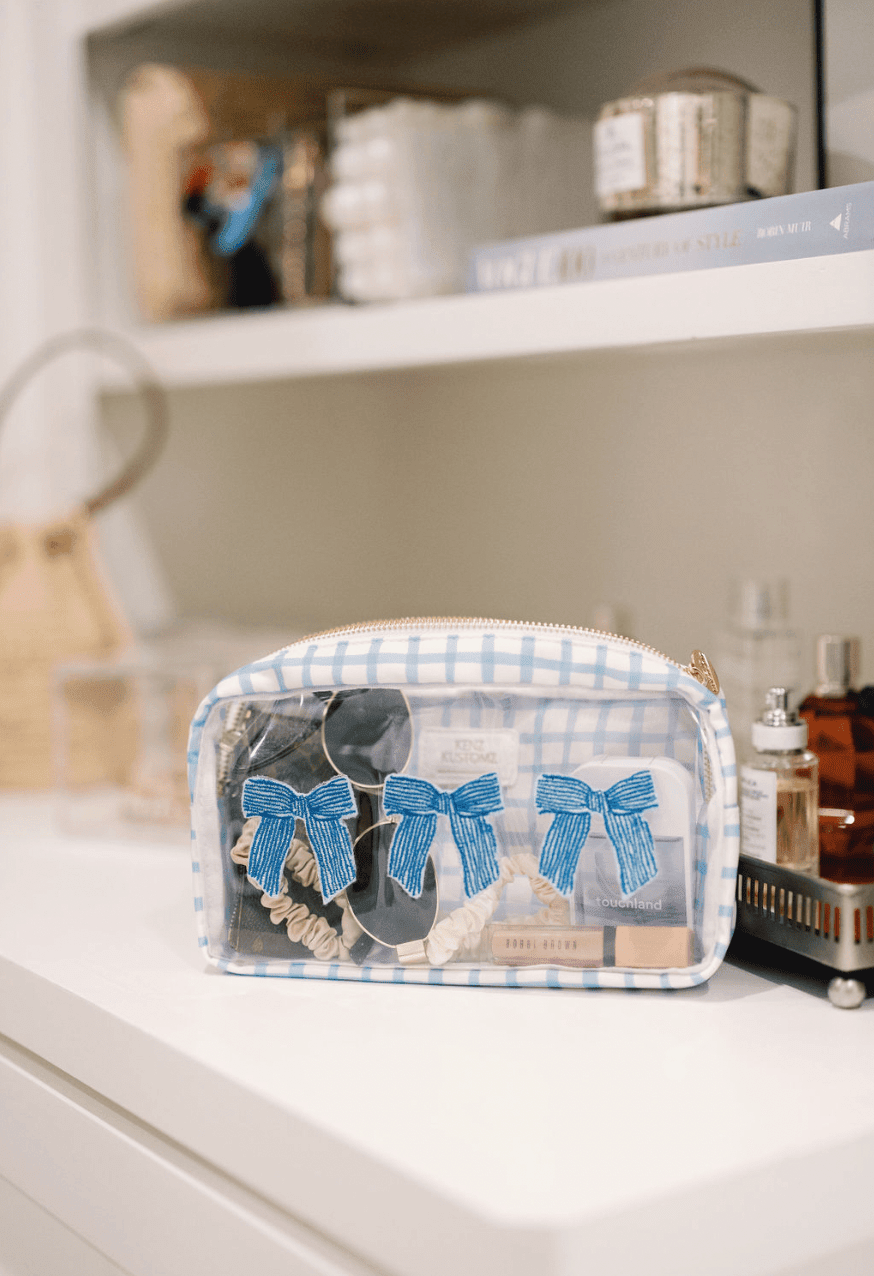 Clear makeup bag with blue gingham trim featuring three blue bow designs, displayed on bathroom counter