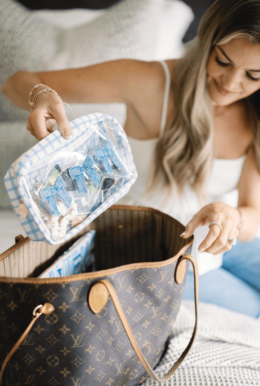 Woman placing blue trellis patterned makeup bag into brown monogram tote bag