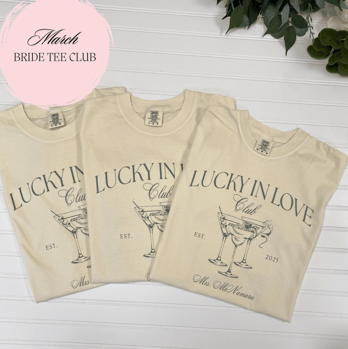 Three cream-colored t-shirts with "Lucky in Love" cocktail glass design and personalized text on chest and sleeve.