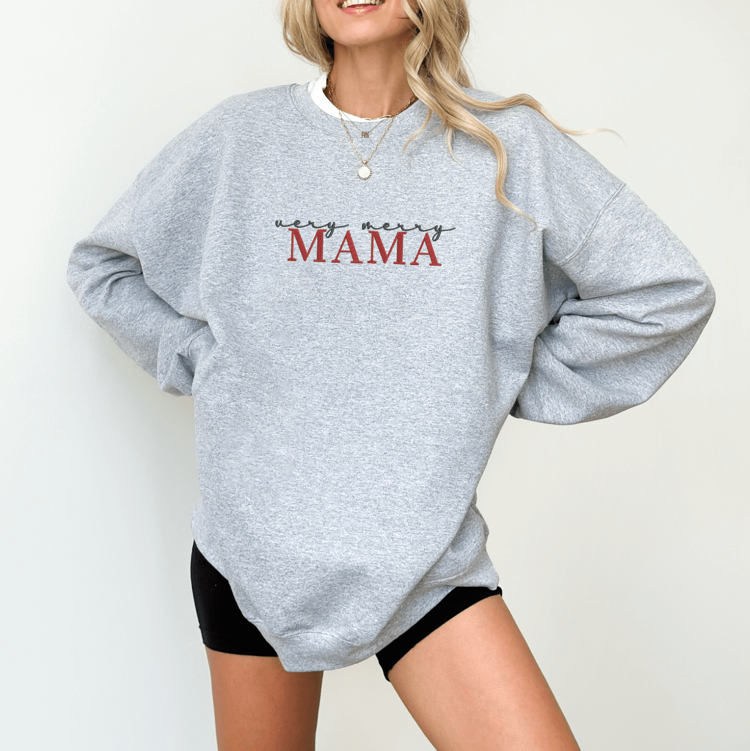 Light gray crewneck sweatshirt with red embroidered "MAMA" text and small festive design details on chest.