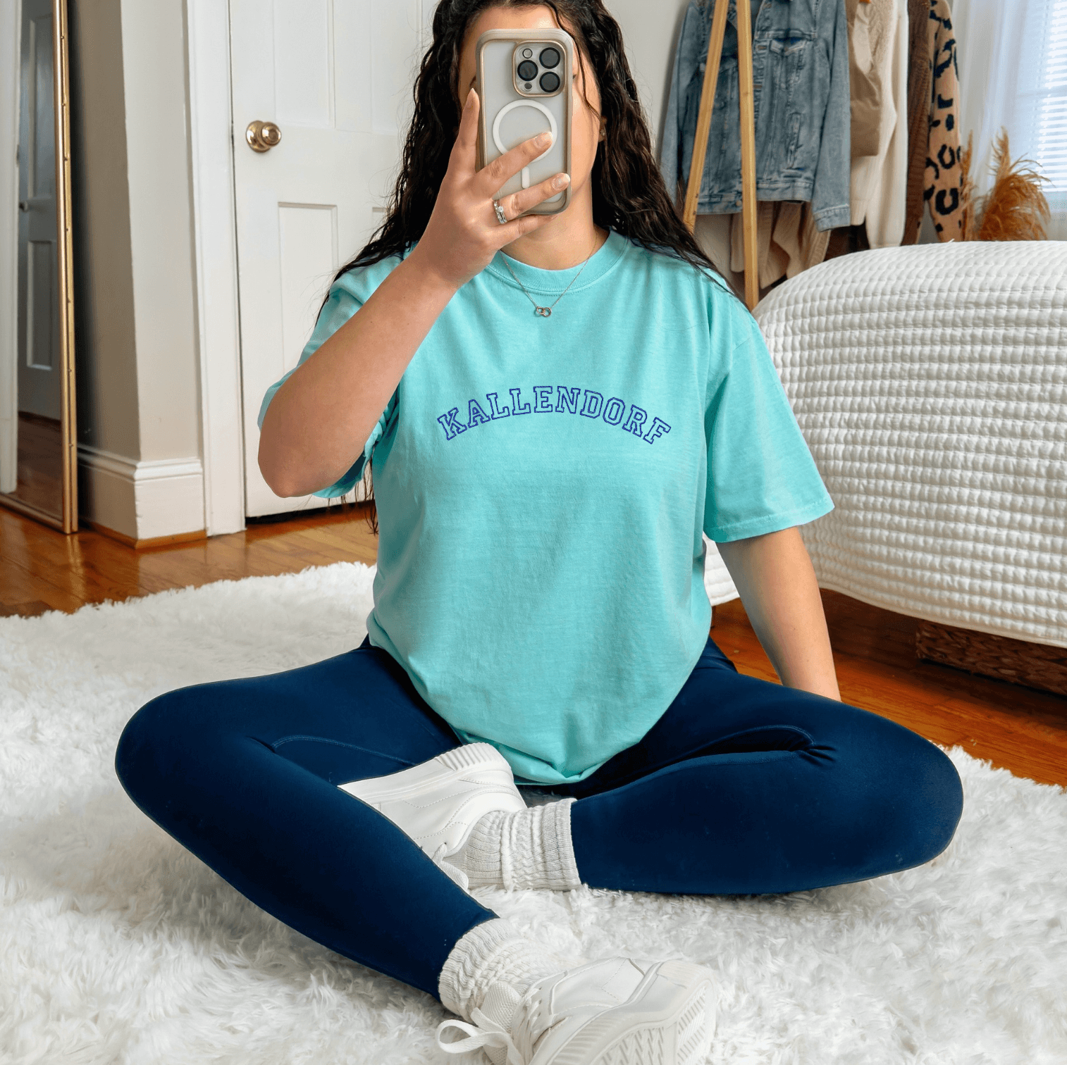 Turquoise t-shirt with embroidered last name across chest, worn by person sitting on white rug indoors