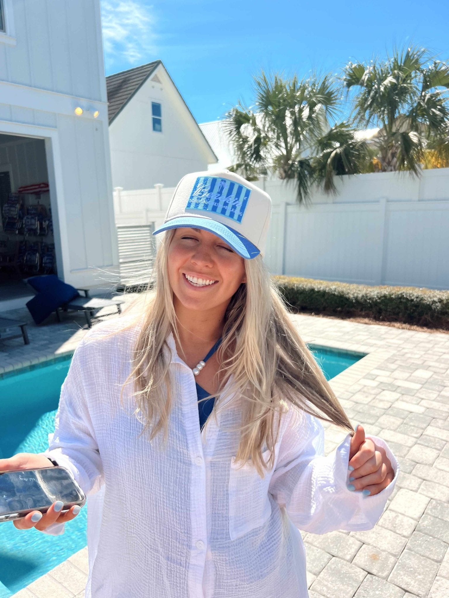 Woman wearing blue and white striped vintage trucker hat with "Beachin'" text, posed by poolside