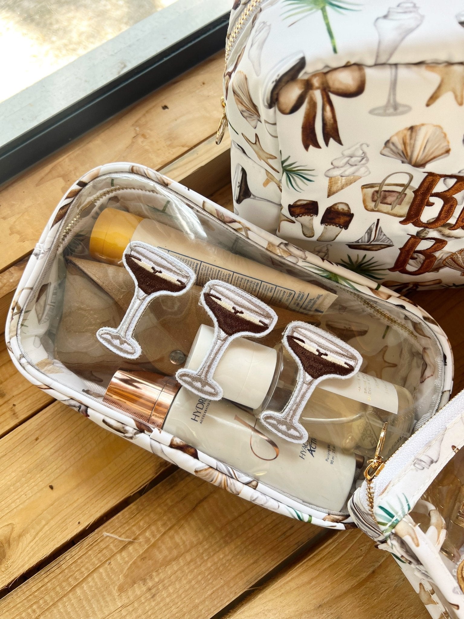 Cream canvas travel bag with cocktail print containing wine glasses and bar tools, displayed on wooden surface.