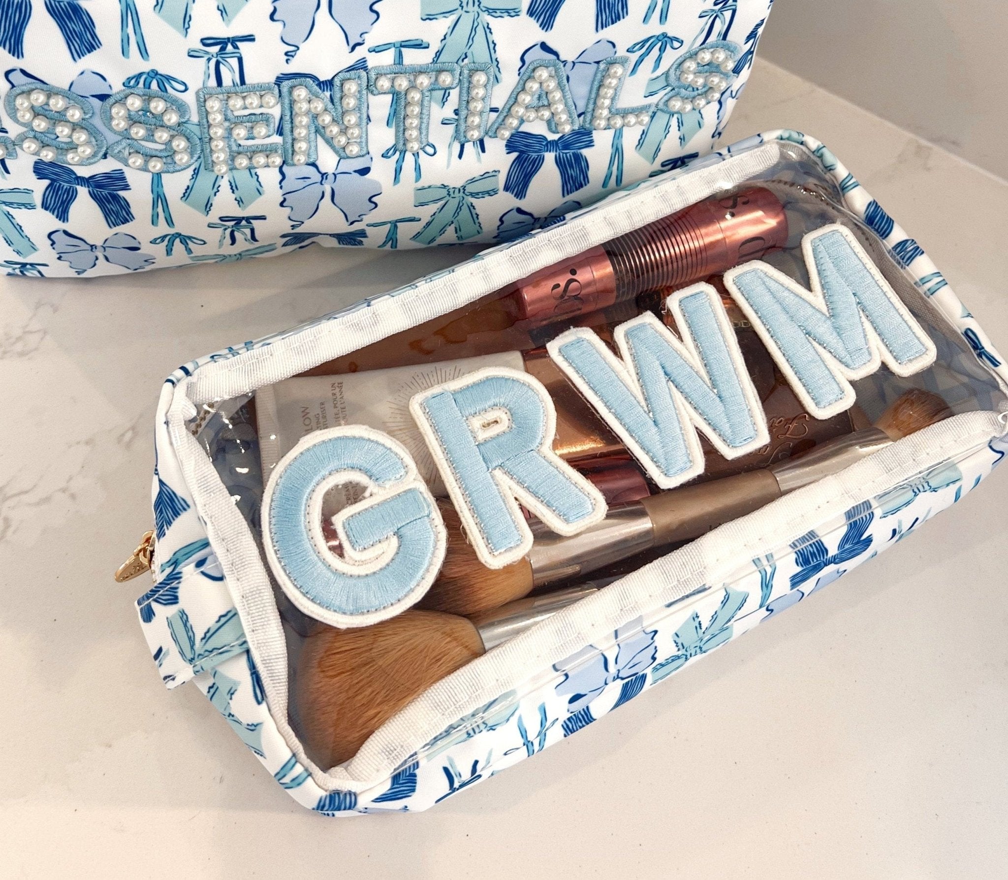 Blue and white patterned makeup bag with "GRWM" text in light blue letters on wooden blocks inside.