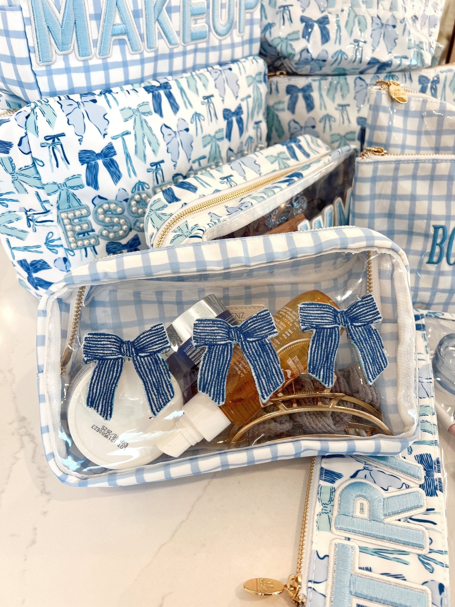 Clear makeup bag with three navy striped bow hair clips inside, displayed with blue and white gingham and bow-patterned packaging.