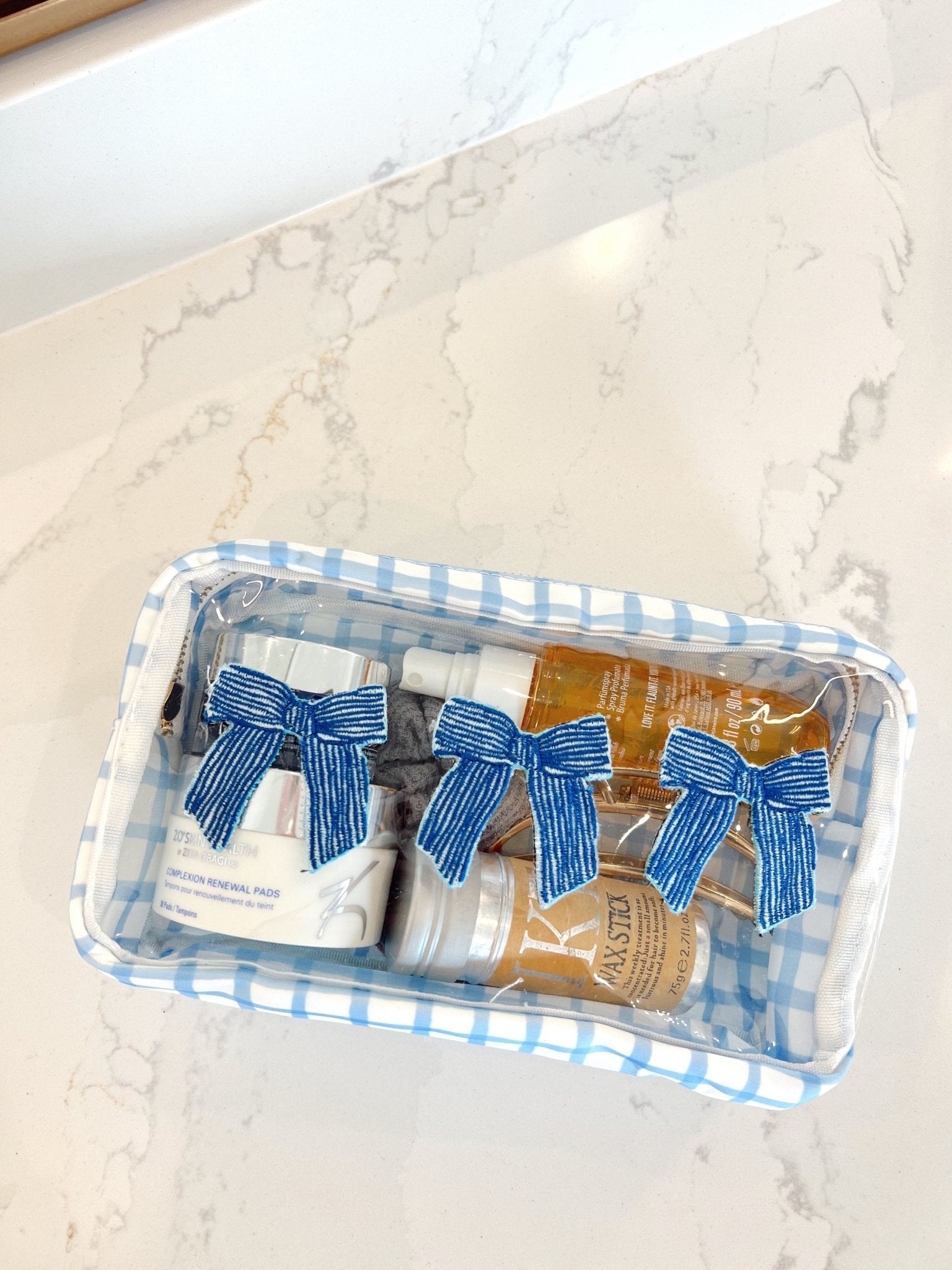 Clear rectangular makeup bag with blue and white gingham pattern, containing three items tied with blue striped bows.