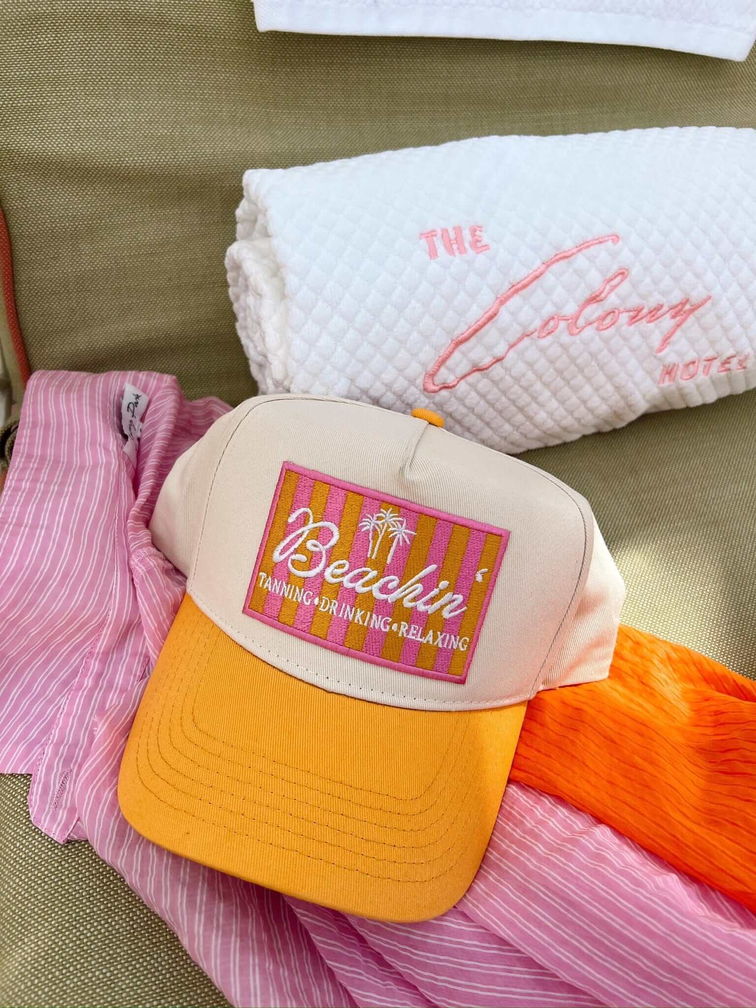 Cream and yellow vintage trucker hat with colorful "Beachin'" graphic patch, displayed on pink and orange fabrics.