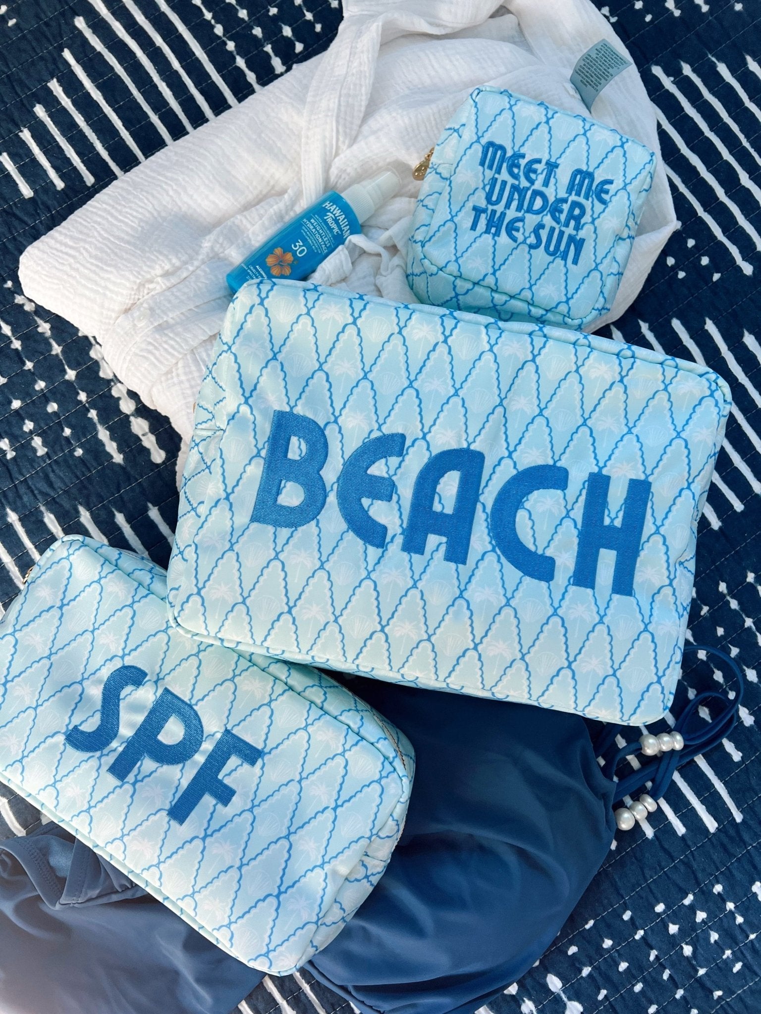 Blue and white mesh makeup bags with "BEACH" text and grid pattern design, displayed with sunscreen bottle