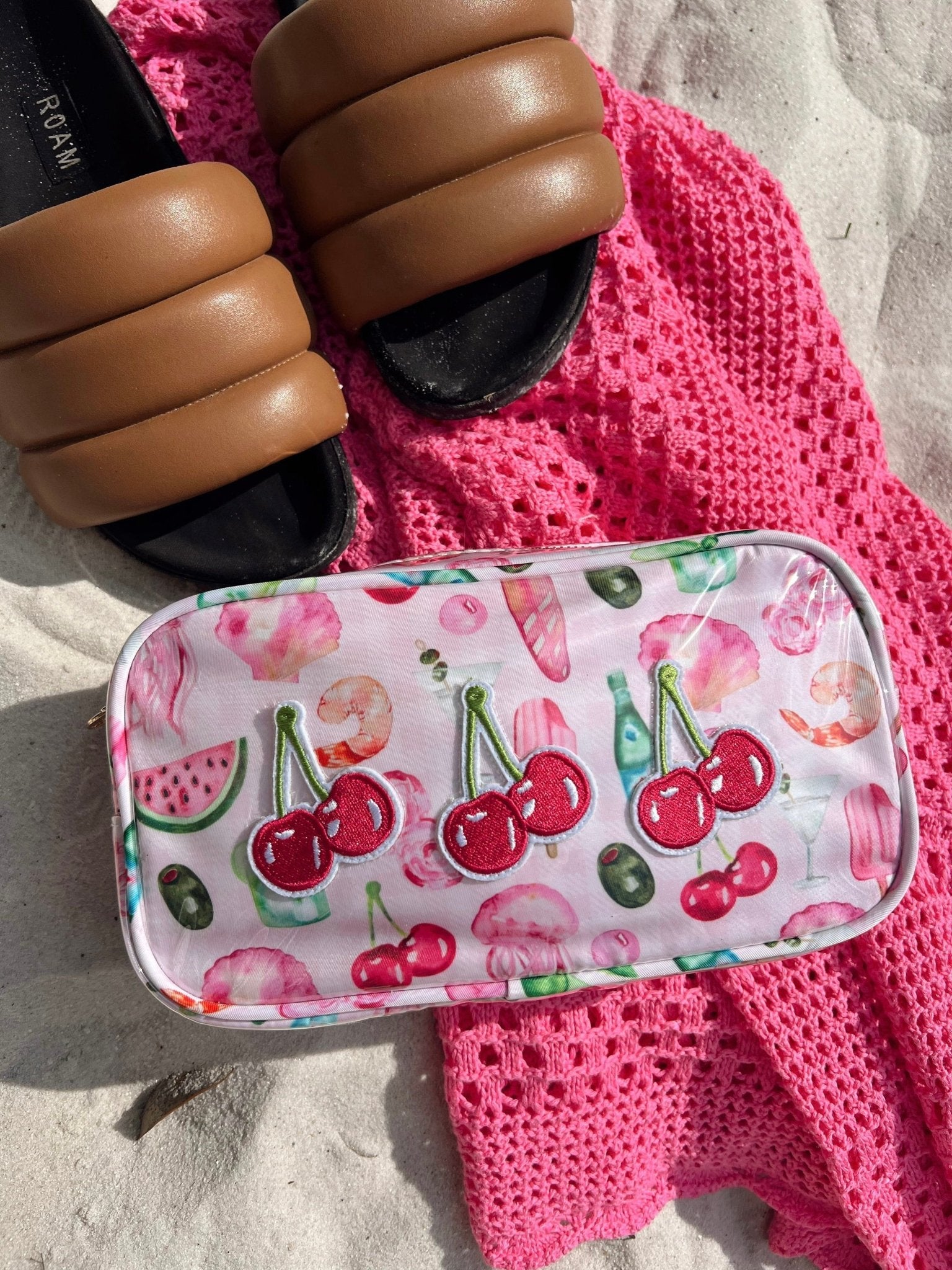 Clear cosmetic bag with cherry and watermelon print design, displayed on pink beach towel