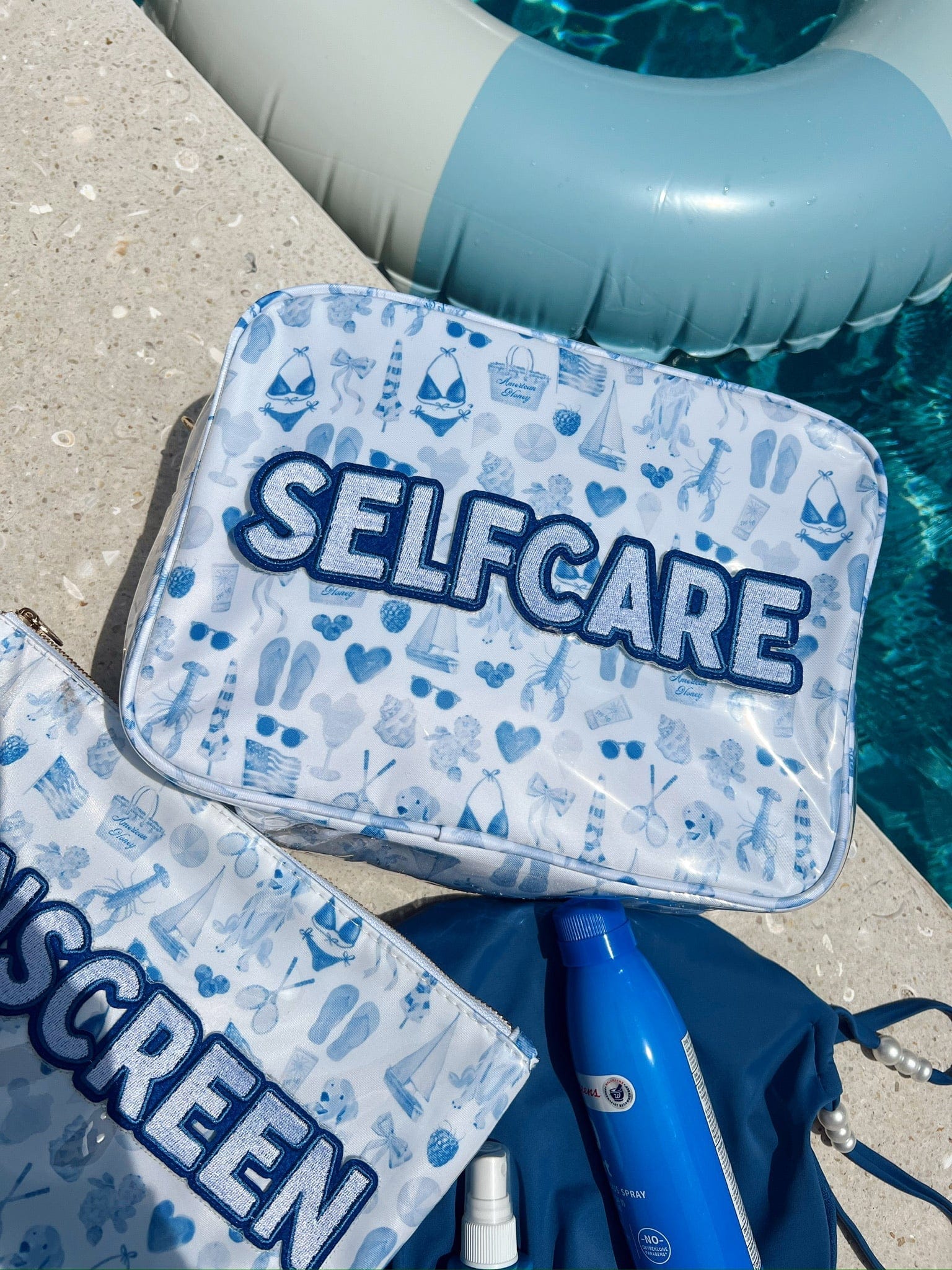 Blue and white patterned makeup bag with "SELFCARE" text, placed poolside next to inflatable float and blue paddle.