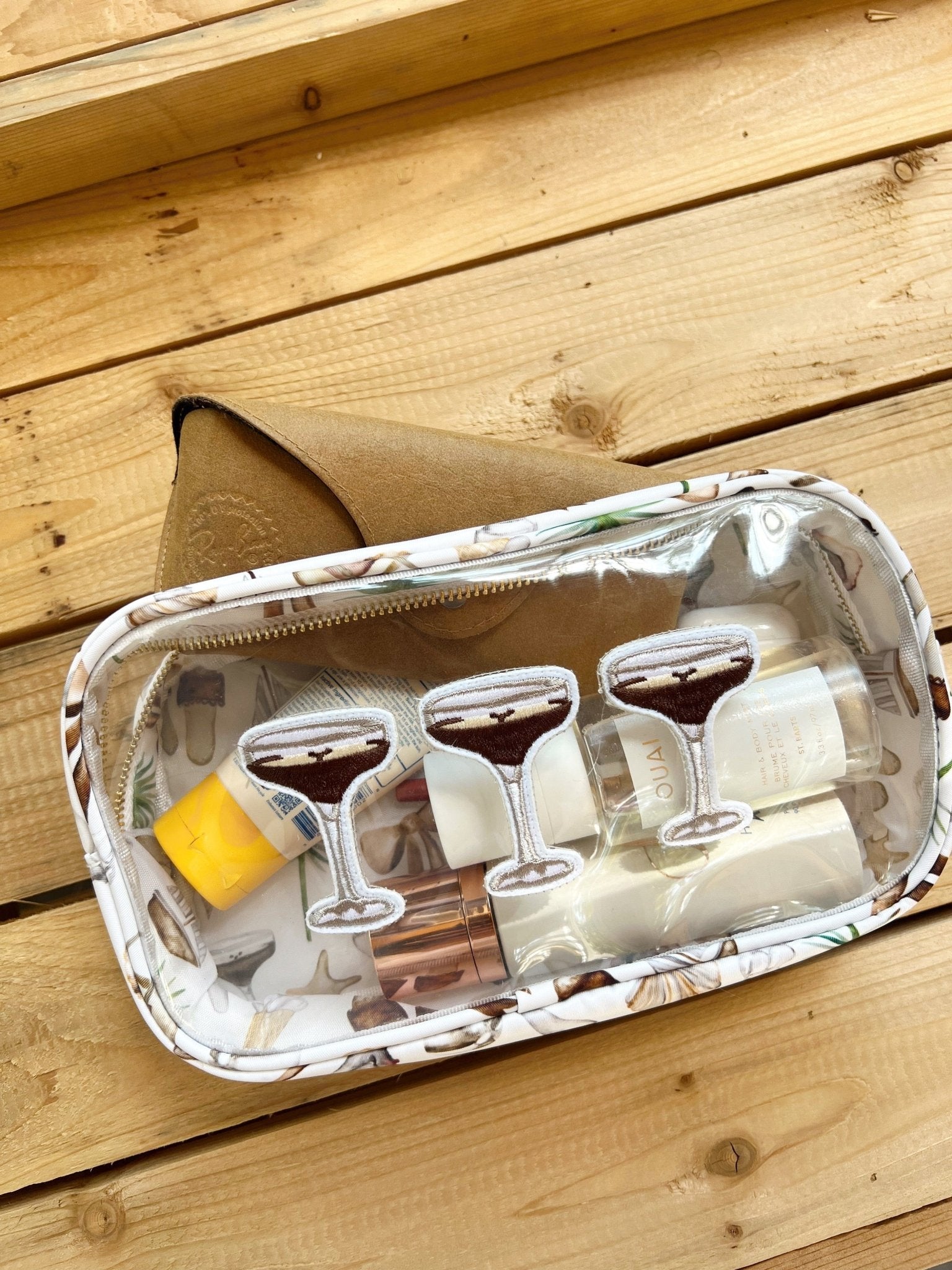 White patterned travel bag with three martini glasses, cocktail napkins, and yellow citrus garnish on wooden deck.