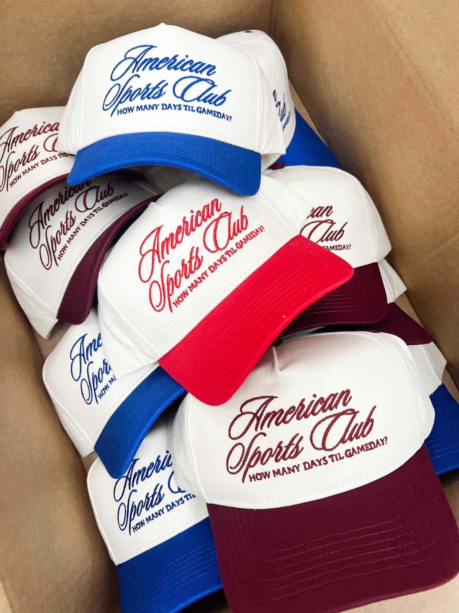 Stack of vintage trucker hats with "American Sports Club" text in blue, red, and burgundy with colored fabric bands.