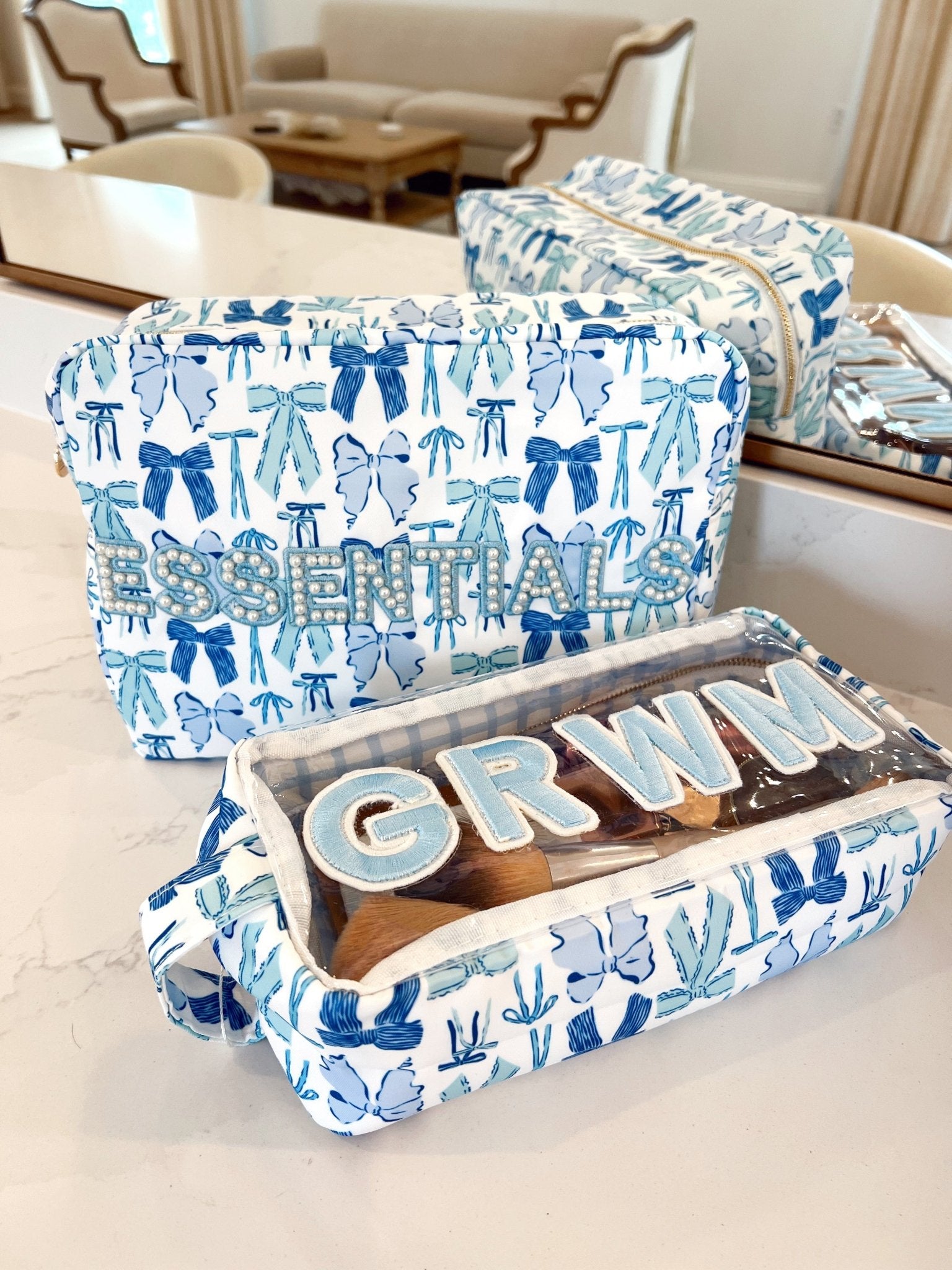 Blue and white patterned makeup bag with bows and decorative elements, displaying personalized "GRWM" lettering inside the open compartment.