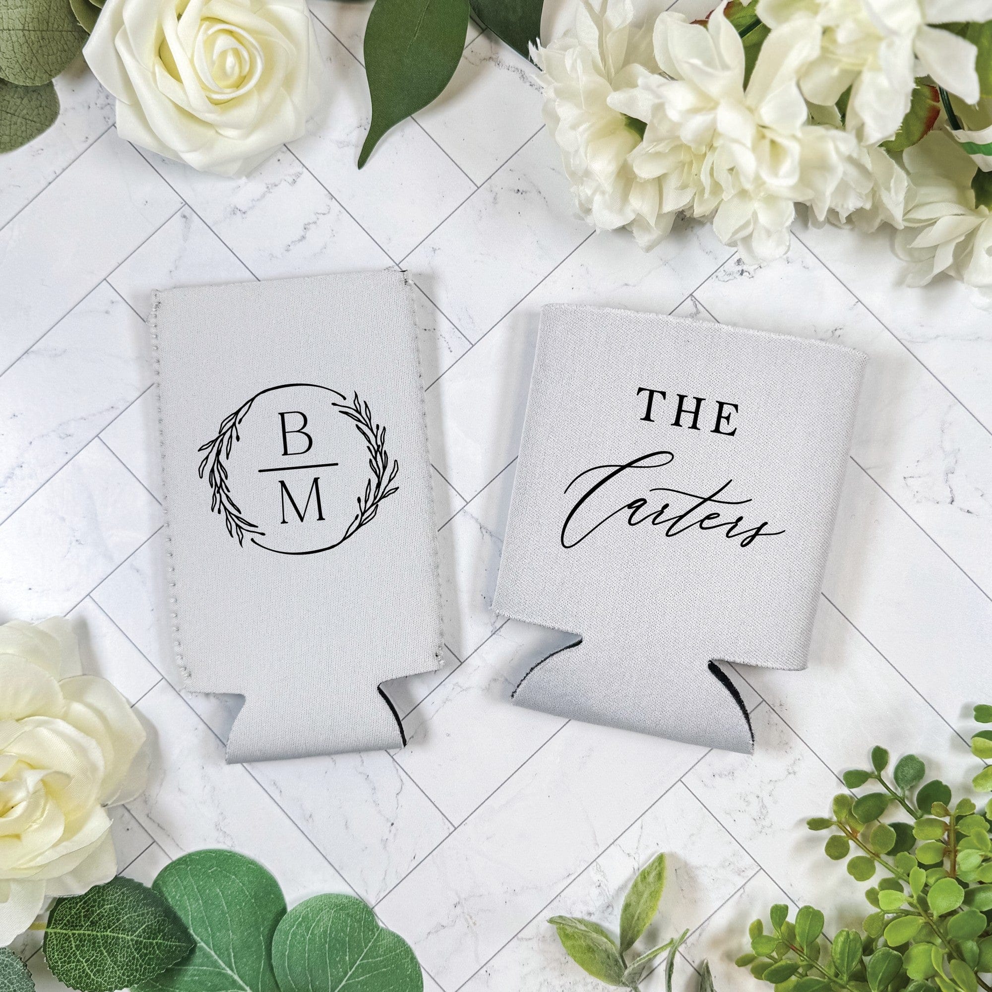 Two personalized light-colored insulated can coolers, featuring a custom monogram design on one and a family name design on the other, ideal for wedding or event beverage insulation.