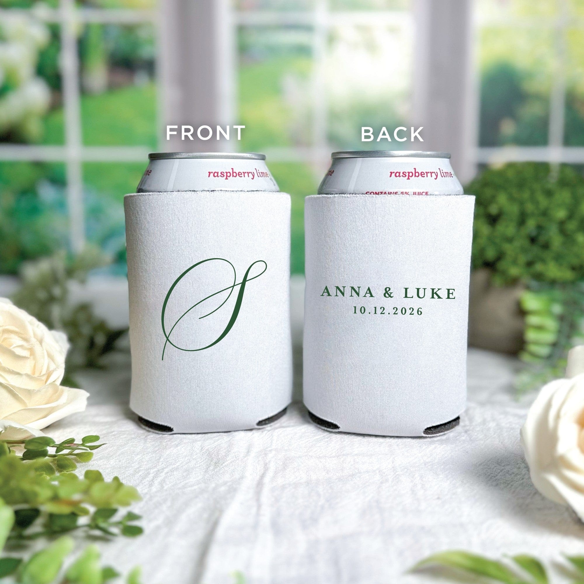 A pair of white fabric can coolers, one featuring a large script initial and the other with two lines of personalized text, designed for wedding or event favors.