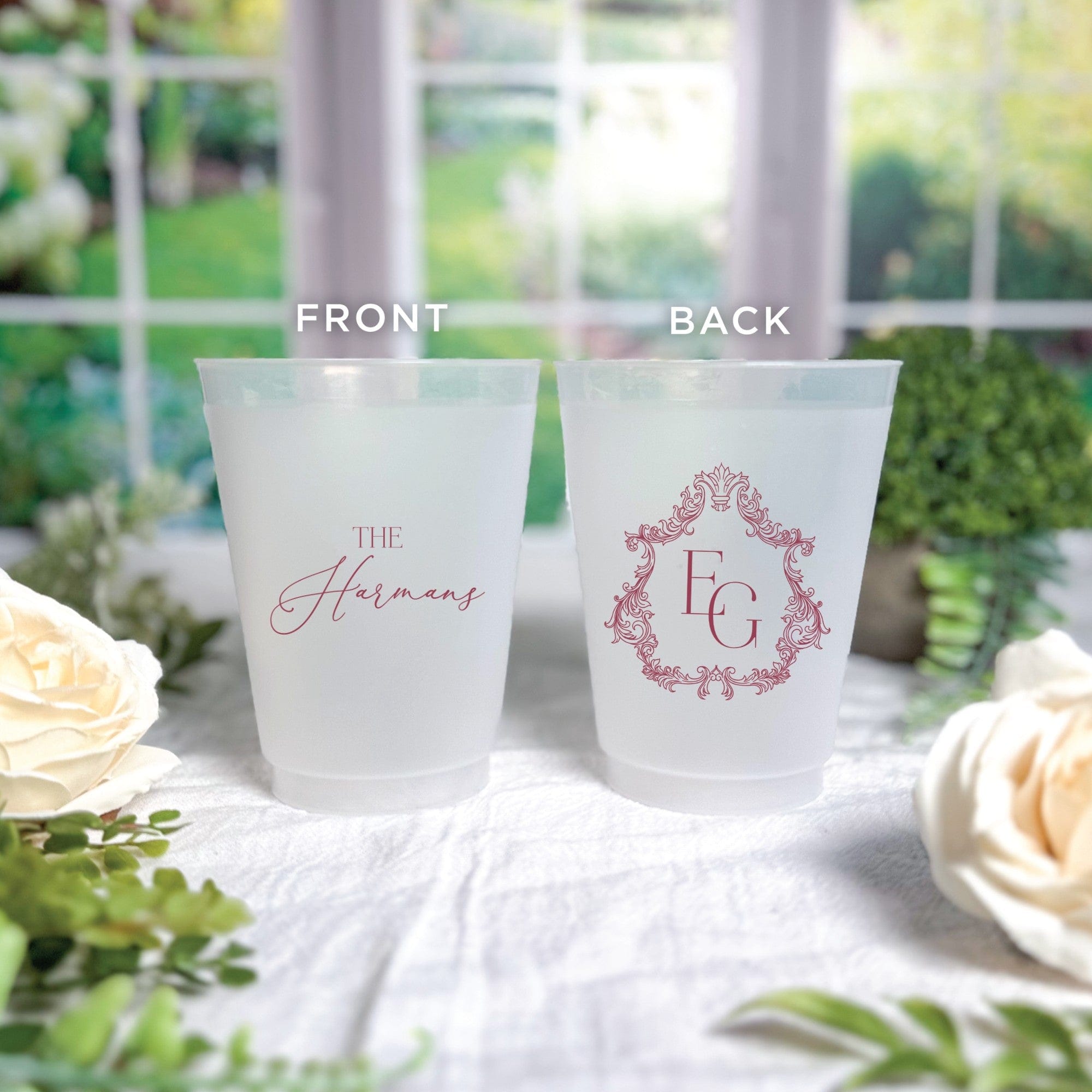Frosted plastic wedding cups featuring personalized designs in a deep red color, showcasing both a custom surname script and an ornate monogram for event drinkware.