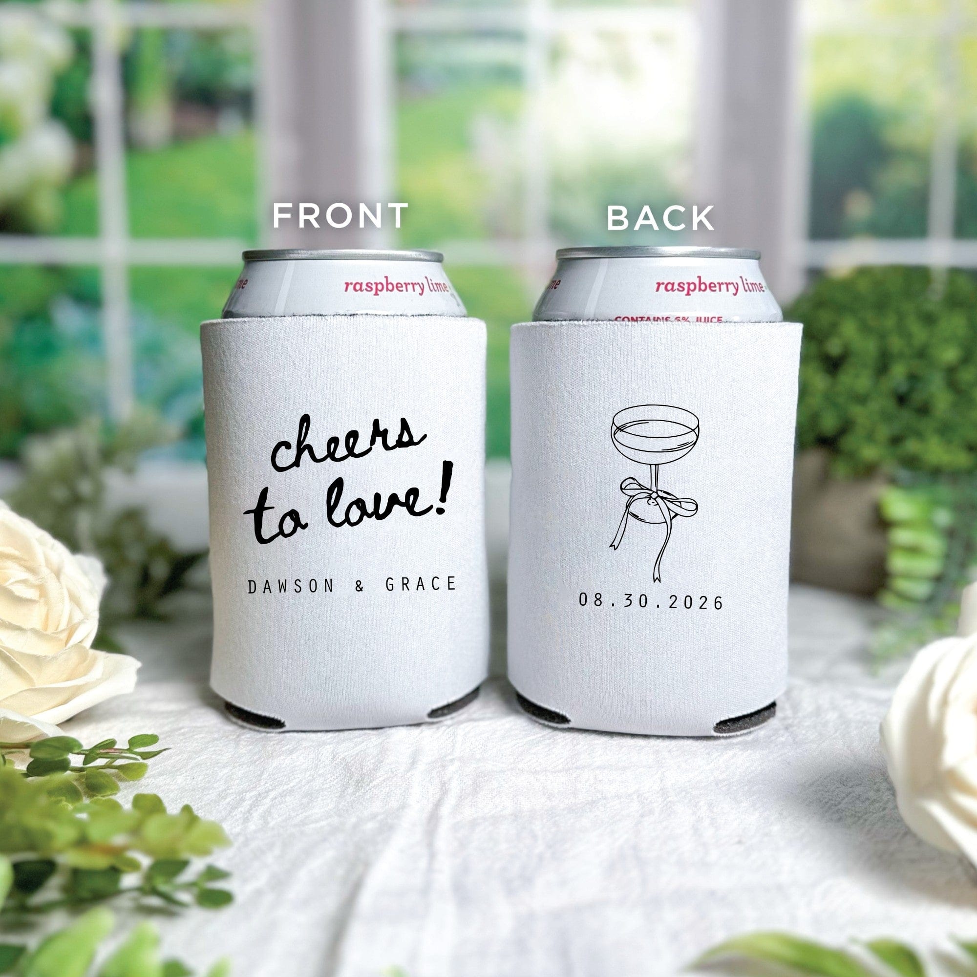 Two white fabric can coolers, one featuring a celebratory phrase in script font and the other a line drawing of a champagne coupe with a bow, designed for wedding or event beverage insulation.