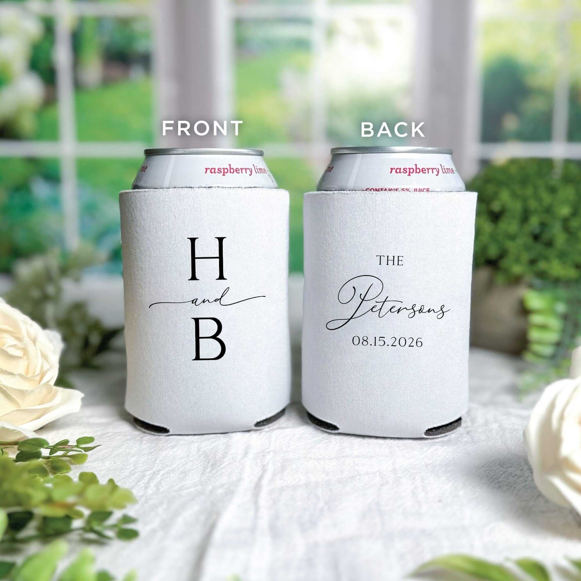 A pair of white fabric can coolers, personalized with elegant black text featuring initials on the front and a celebratory message on the back, ideal for wedding or event favors.