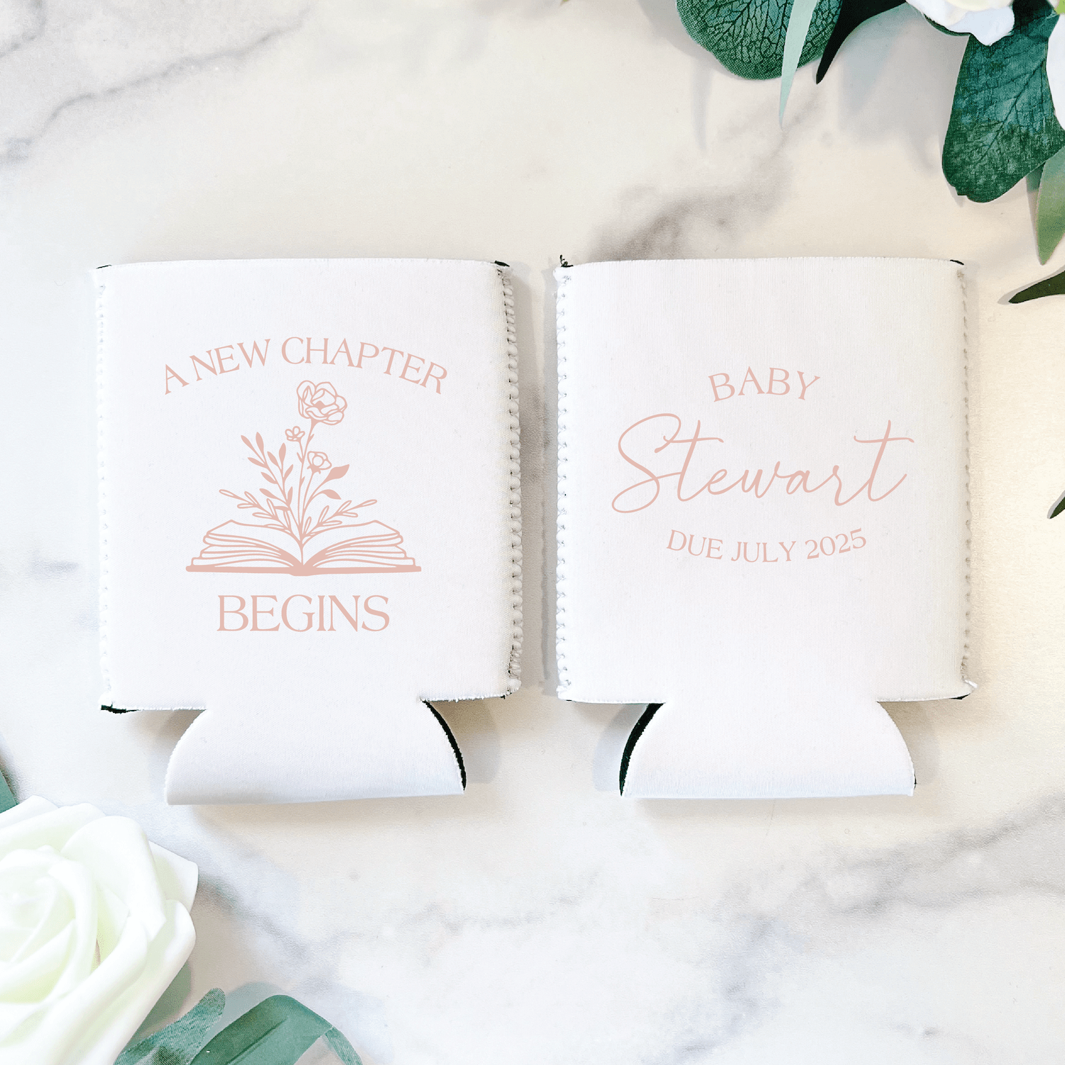 Two white can coolers with rose gold text and book design, one reading "A New Chapter Begins" and the other "Baby Stewart Due July 2025"