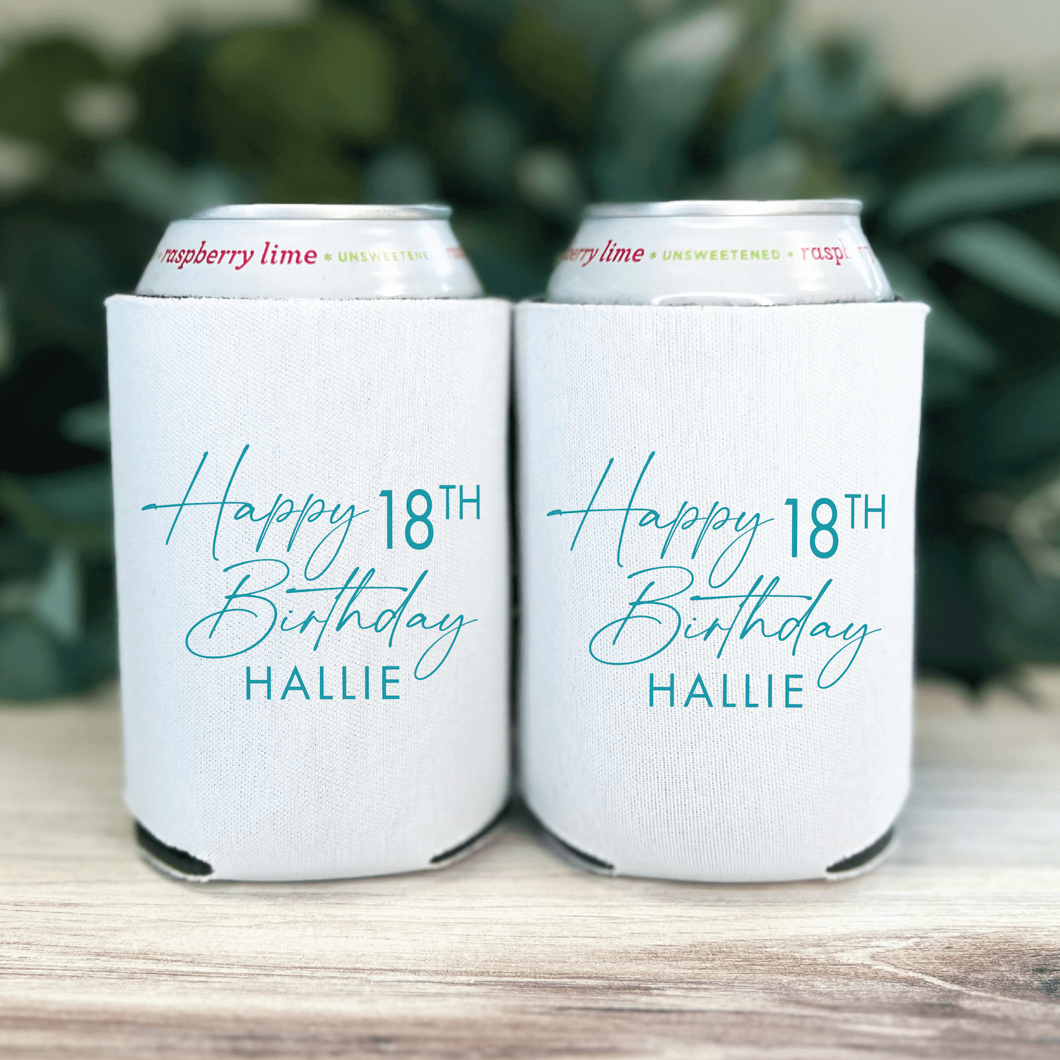 White can coolers with teal cursive text reading "Happy 18TH Birthday HALLIE" personalization, displayed as a pair on wood surface with greenery backdrop.