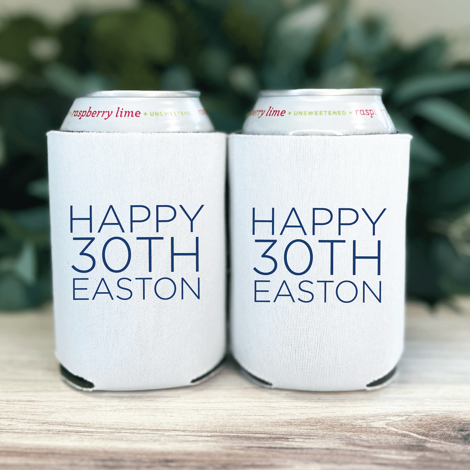 Two white can coolers with "Happy 30th Easton" printed in blue text, holding cans with raspberry lime labels.