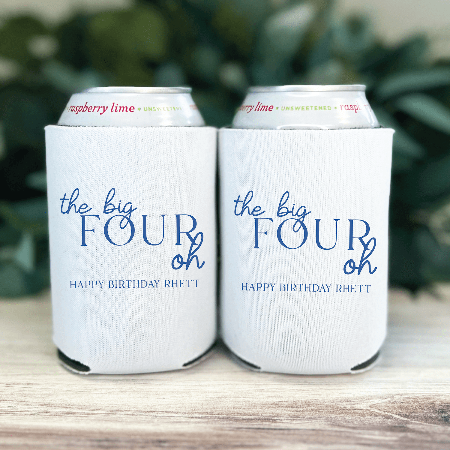 White can coolers with blue text reading "the big FOUR oh" and "HAPPY BIRTHDAY RHETT" personalization, holding canned beverages.