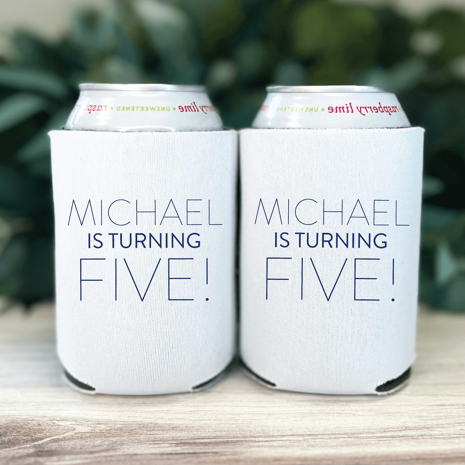 Two white can coolers with "MICHAEL IS TURNING FIVE!" text printed in blue, displayed side by side holding cans.