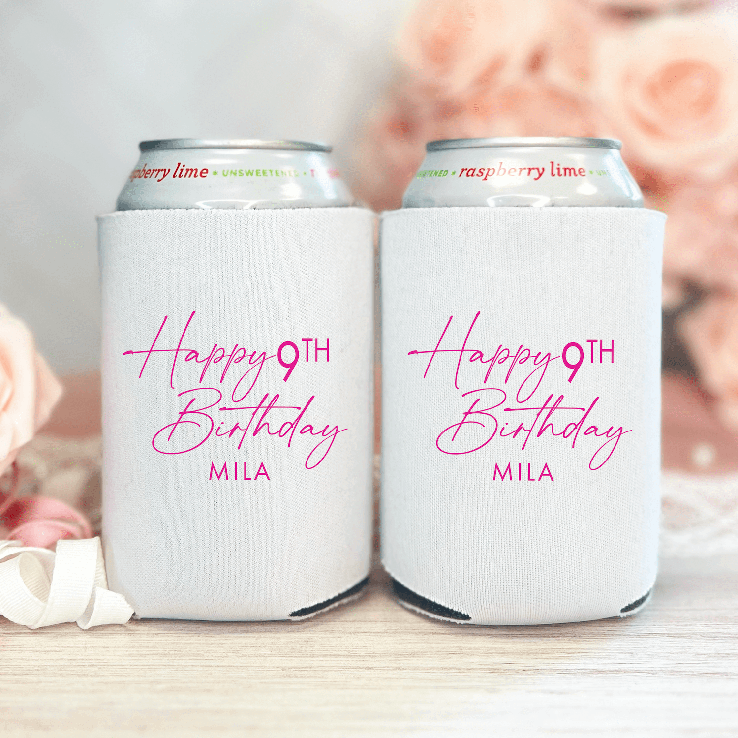 White can coolers with pink script text reading "Happy 9TH Birthday MILA" holding cans, displayed with flowers