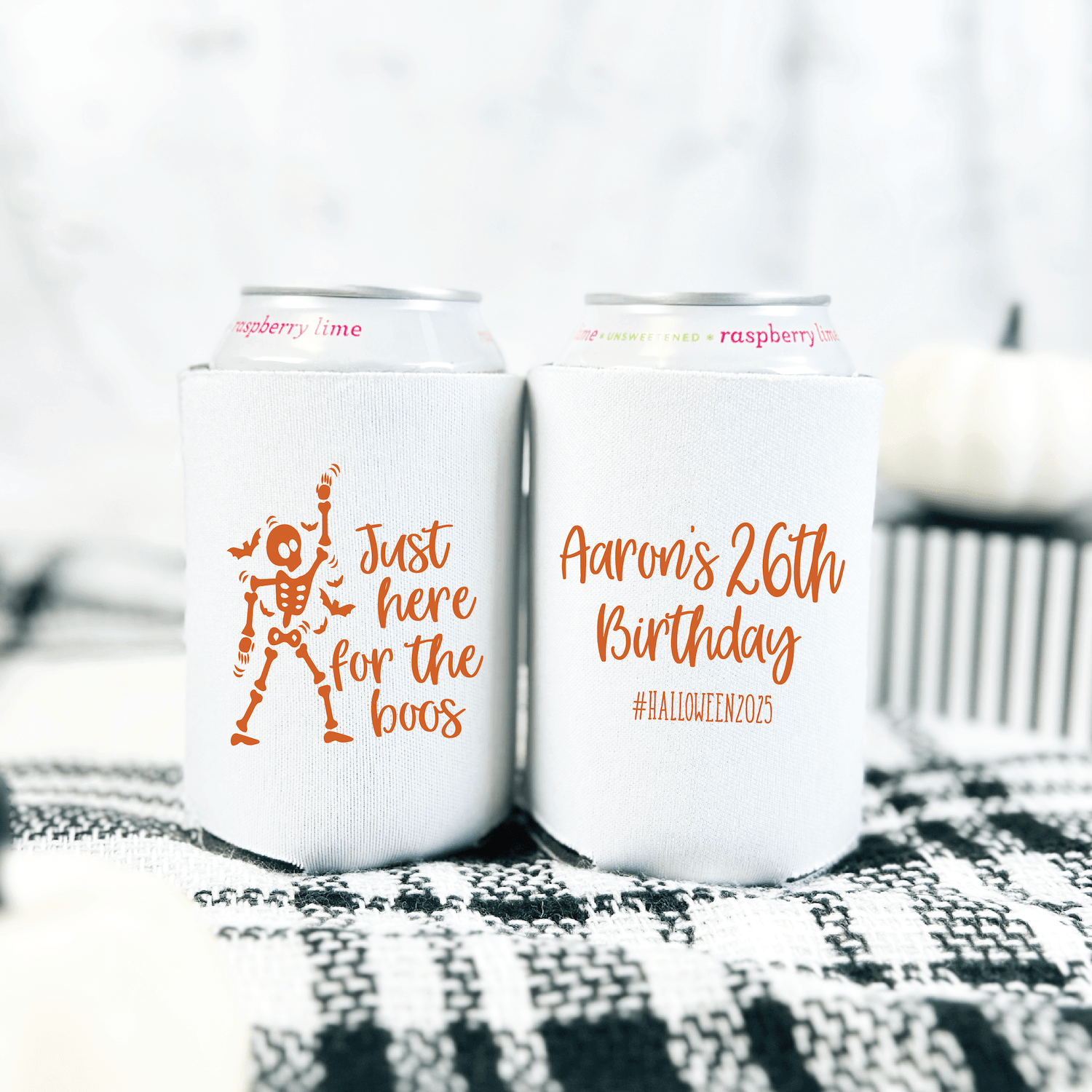 White can coolers with orange text reading "just here for the boos" and "Aaron's 26th Birthday" with hashtag, displayed on patterned fabric.
