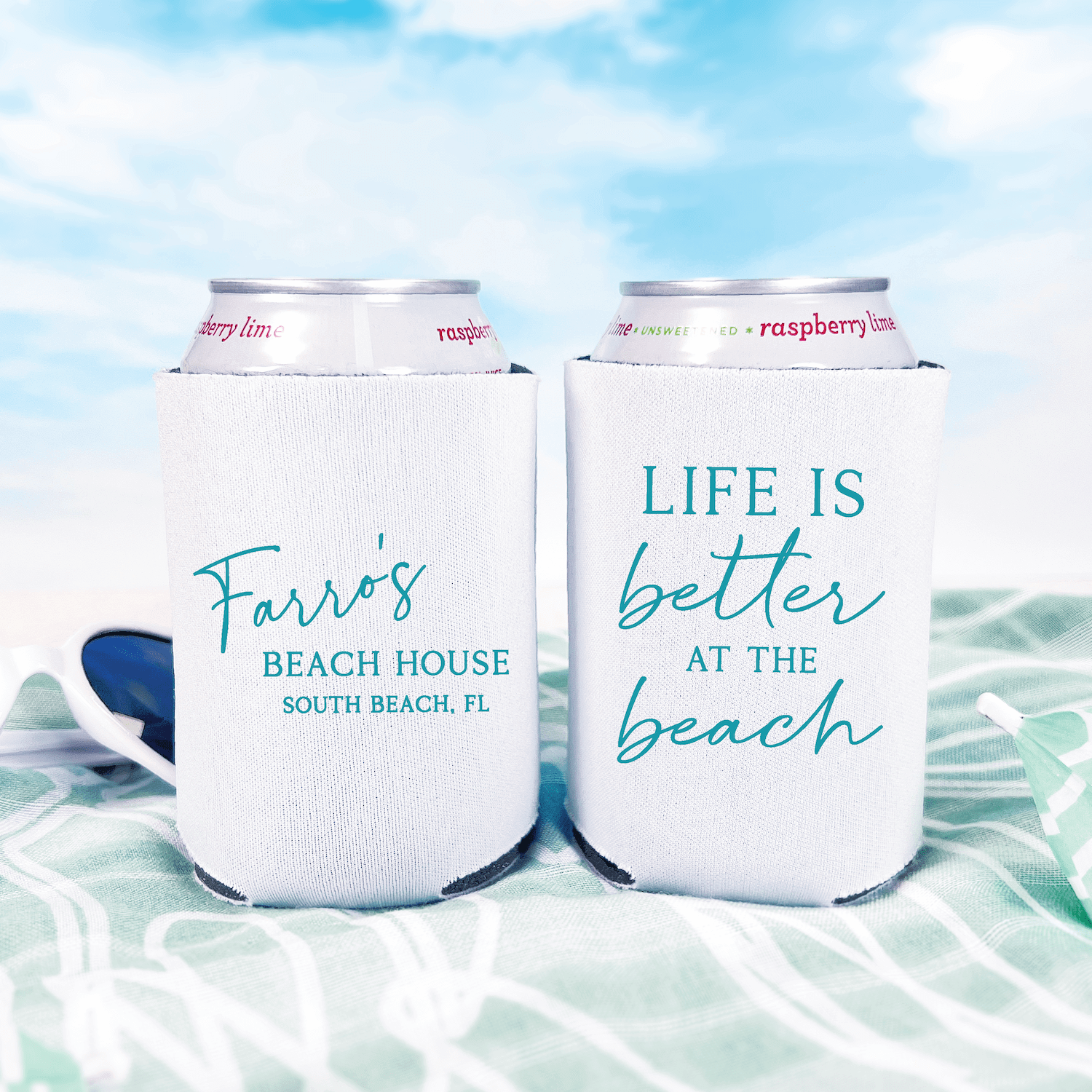 Two white can coolers with turquoise text, one reading "Faye's Beach House South Beach, FL" and the other "Life is better at the beach," holding canned beverages against a beach backdrop.