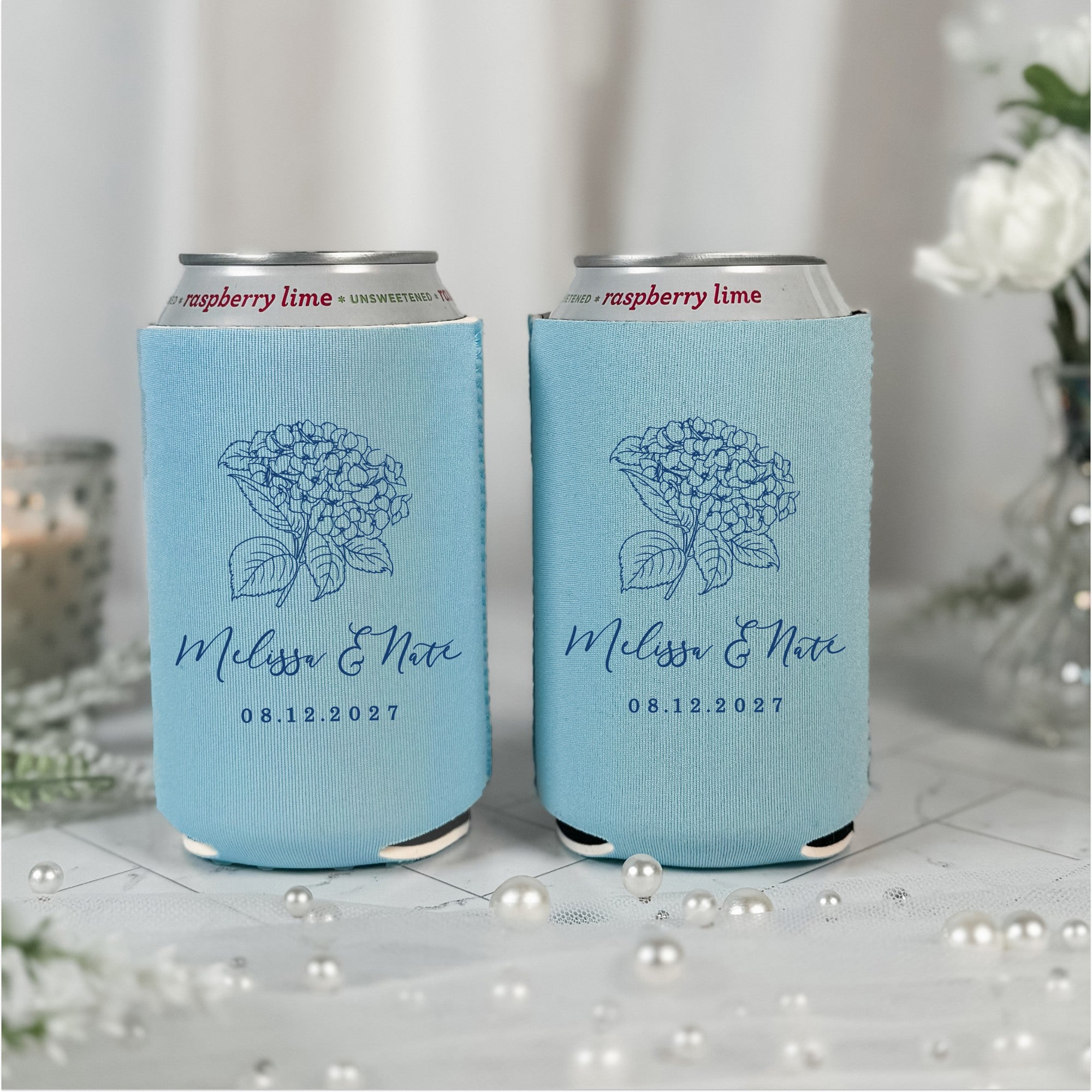 Two light blue neoprene can coolers featuring a detailed dark blue outline illustration of a hydrangea, designed as personalized wedding event decor.