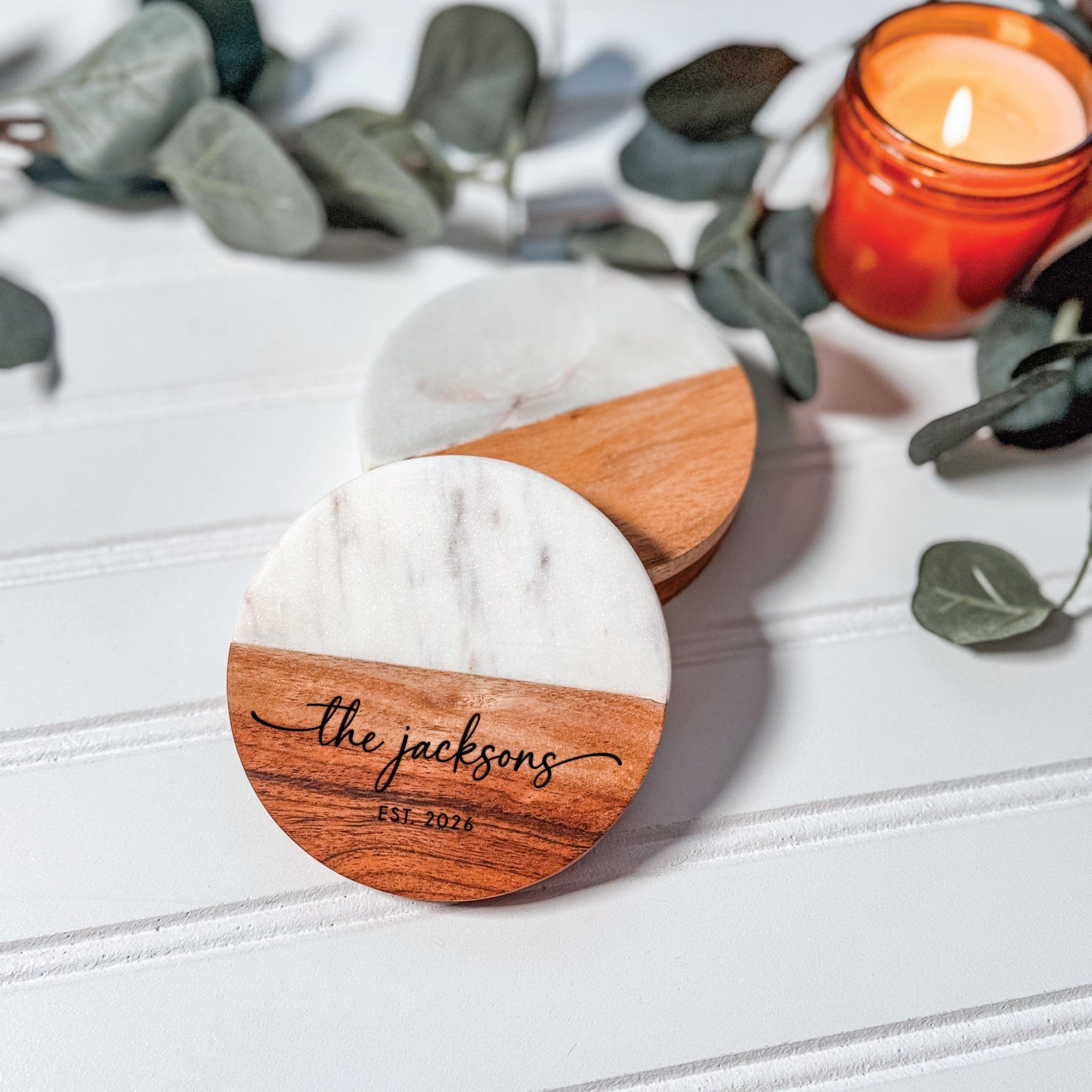 Two round coasters, each featuring a half white marble and half natural wood design, with custom engraving on the wood, serving as elegant wedding decor or favors.