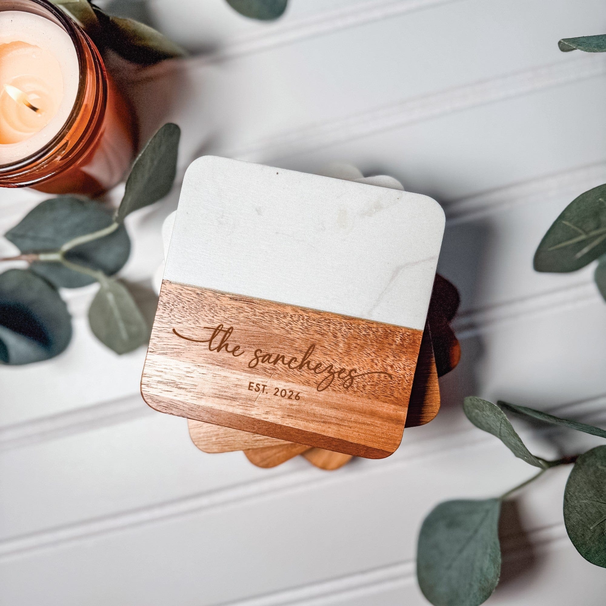 A stack of personalized wedding coasters featuring a square design crafted from white marble and natural wood, with the wood section engraved with a custom design for a unique touch.