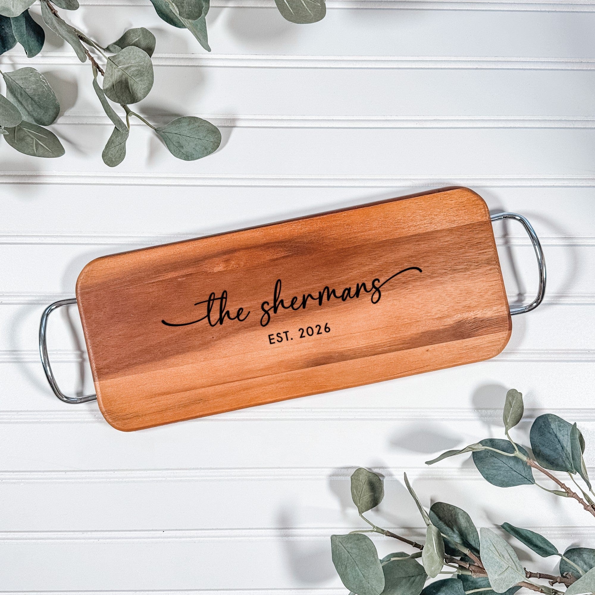 A rectangular light brown wooden serving board featuring sleek silver metal handles on each end, personalized with custom engraving, perfect for wedding or home decor.