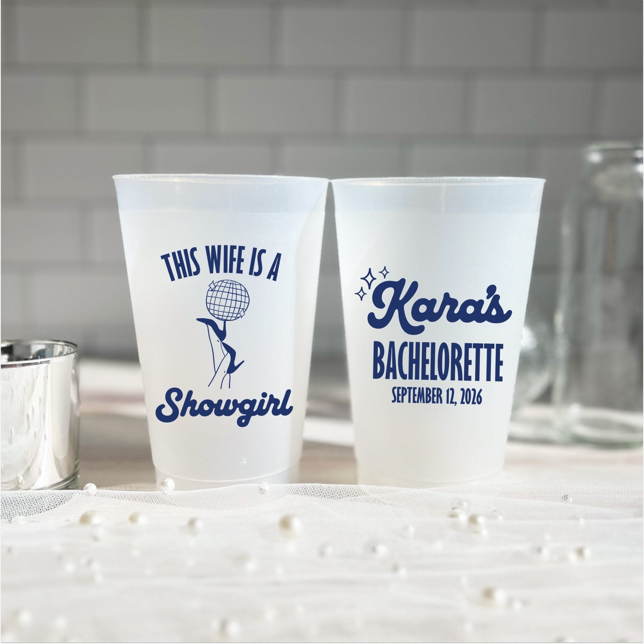 This Wife Is A Showgirl personalized bachelorette party cups - frosted shatterproof cups with navy disco ball design and custom bachelorette name and date, styled with pearls on a light background
