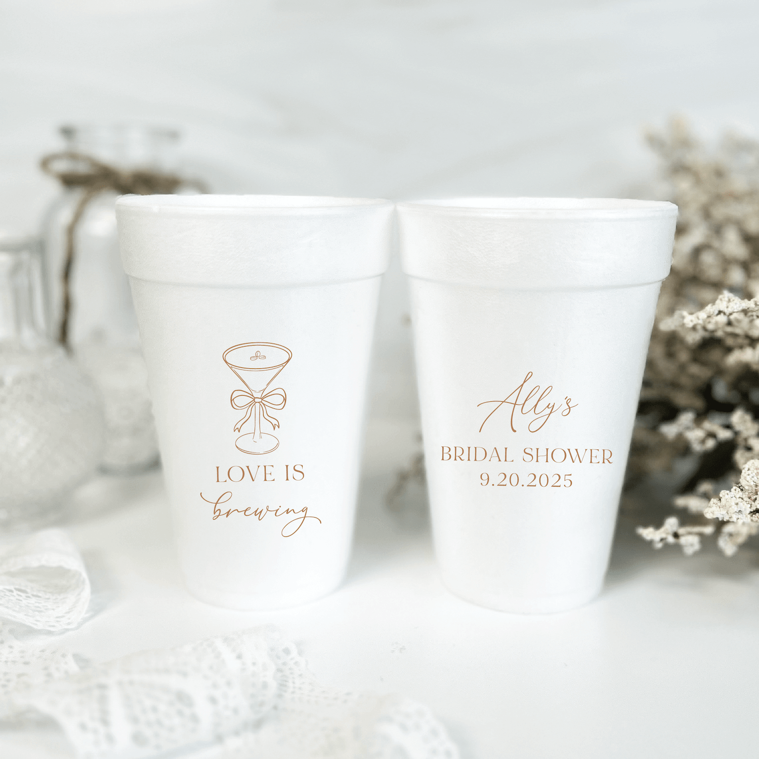 Two white foam cups with rose gold text, one reading "Love Is Brewing" with a coffee cup design, the other saying "Alys Bridal Shower 9.20.2025"