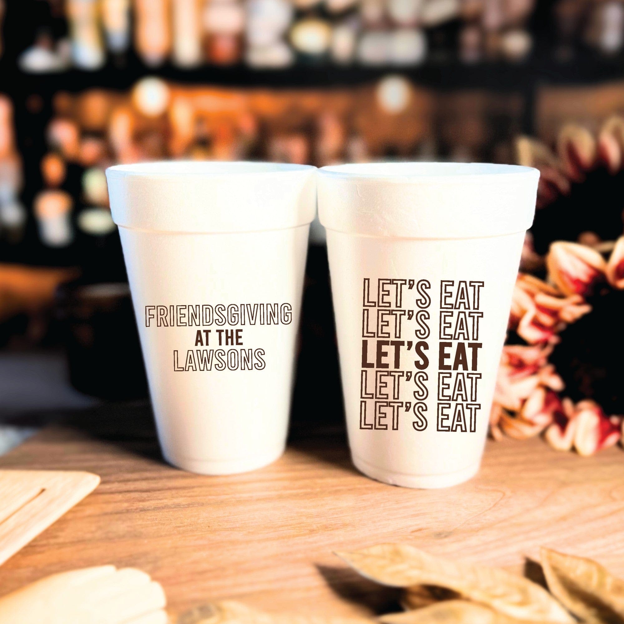 Two white personalized foam cups are displayed on a wooden surface, designed for a festive gathering such as Thanksgiving.