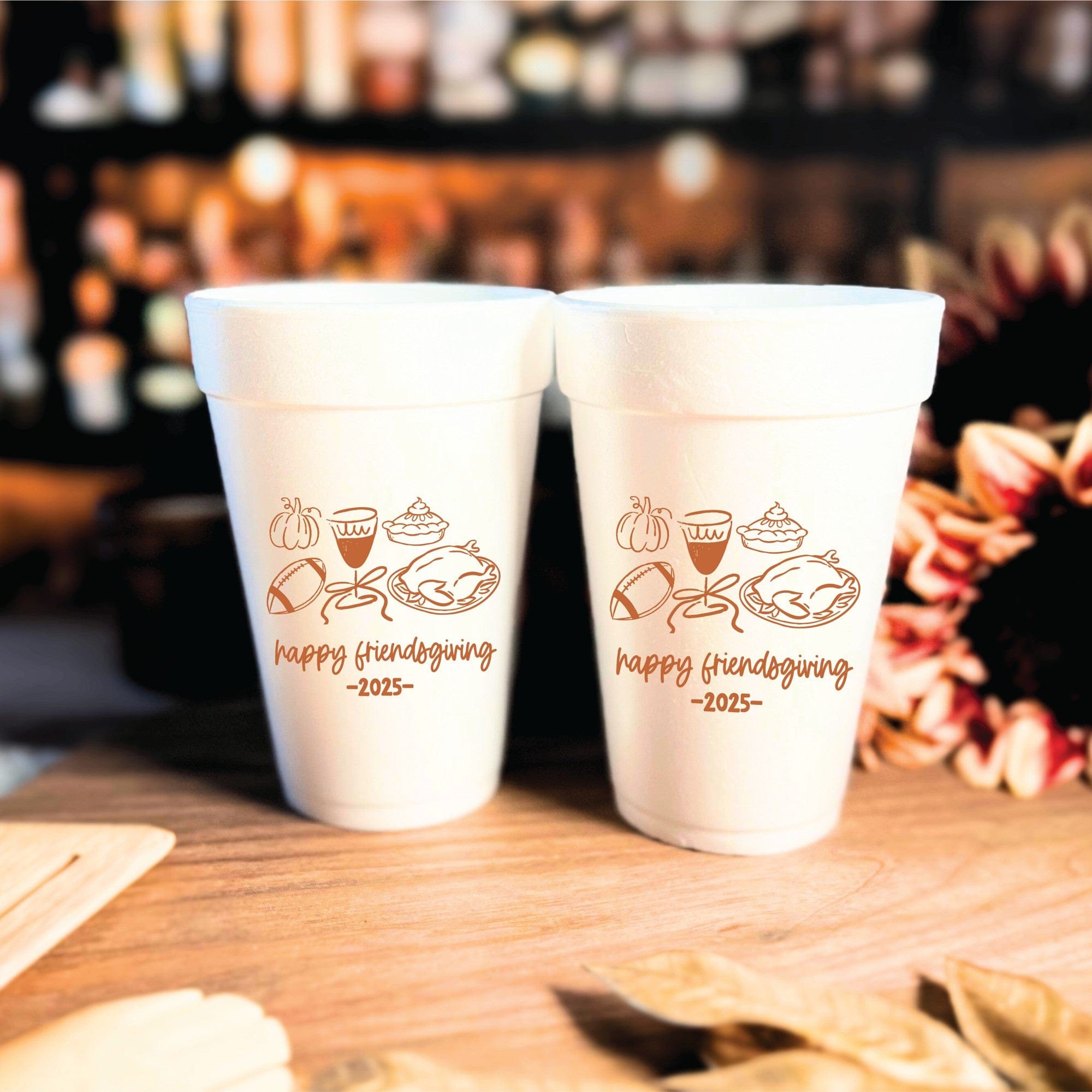 Two white foam cups with a brown custom design featuring autumn and feast-related illustrations, ideal for a Friendsgiving or fall celebration.
