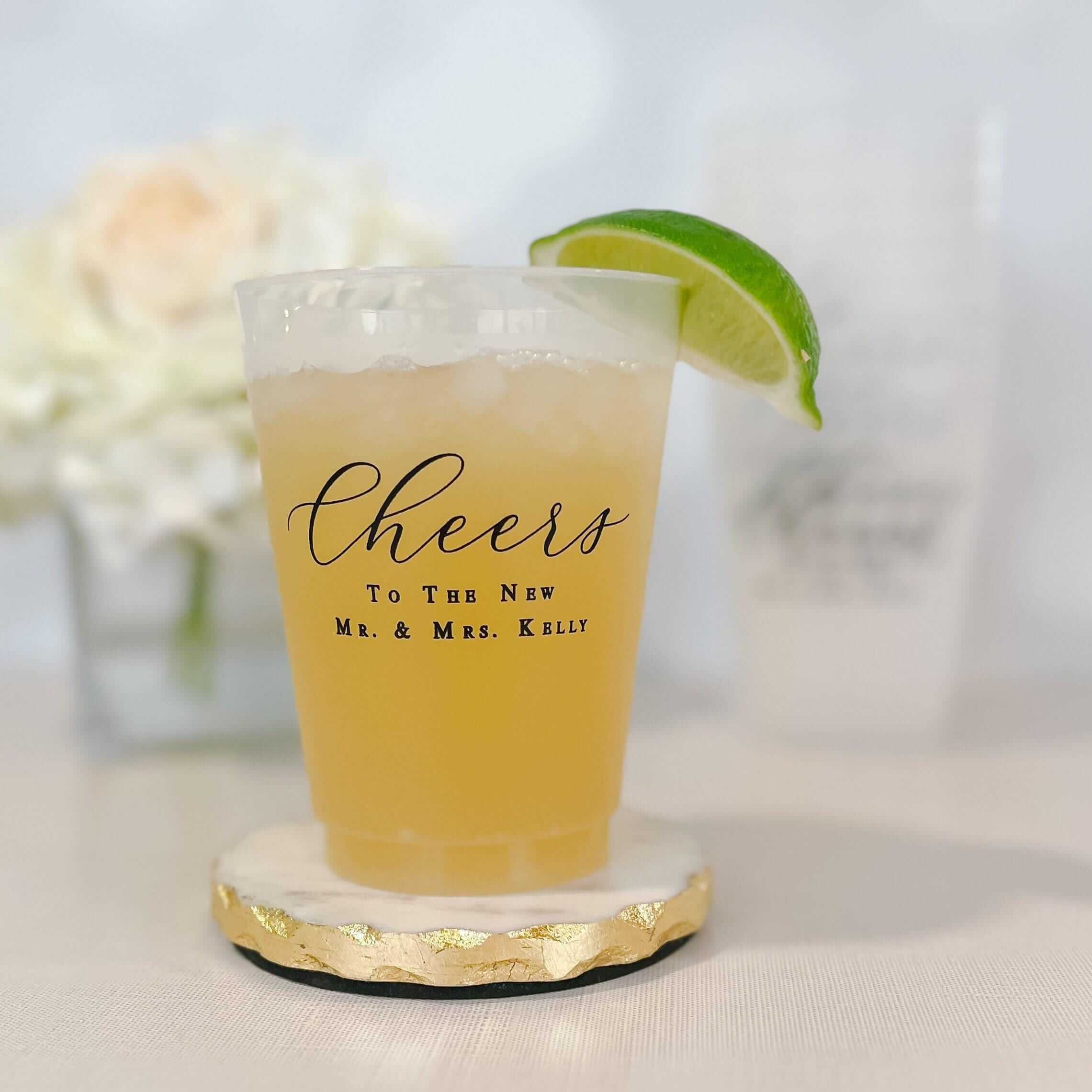 Frosted cup with "Cheers To The New Mr. & Mrs. Kelly" text, filled with pale yellow beverage and lime wedge garnish