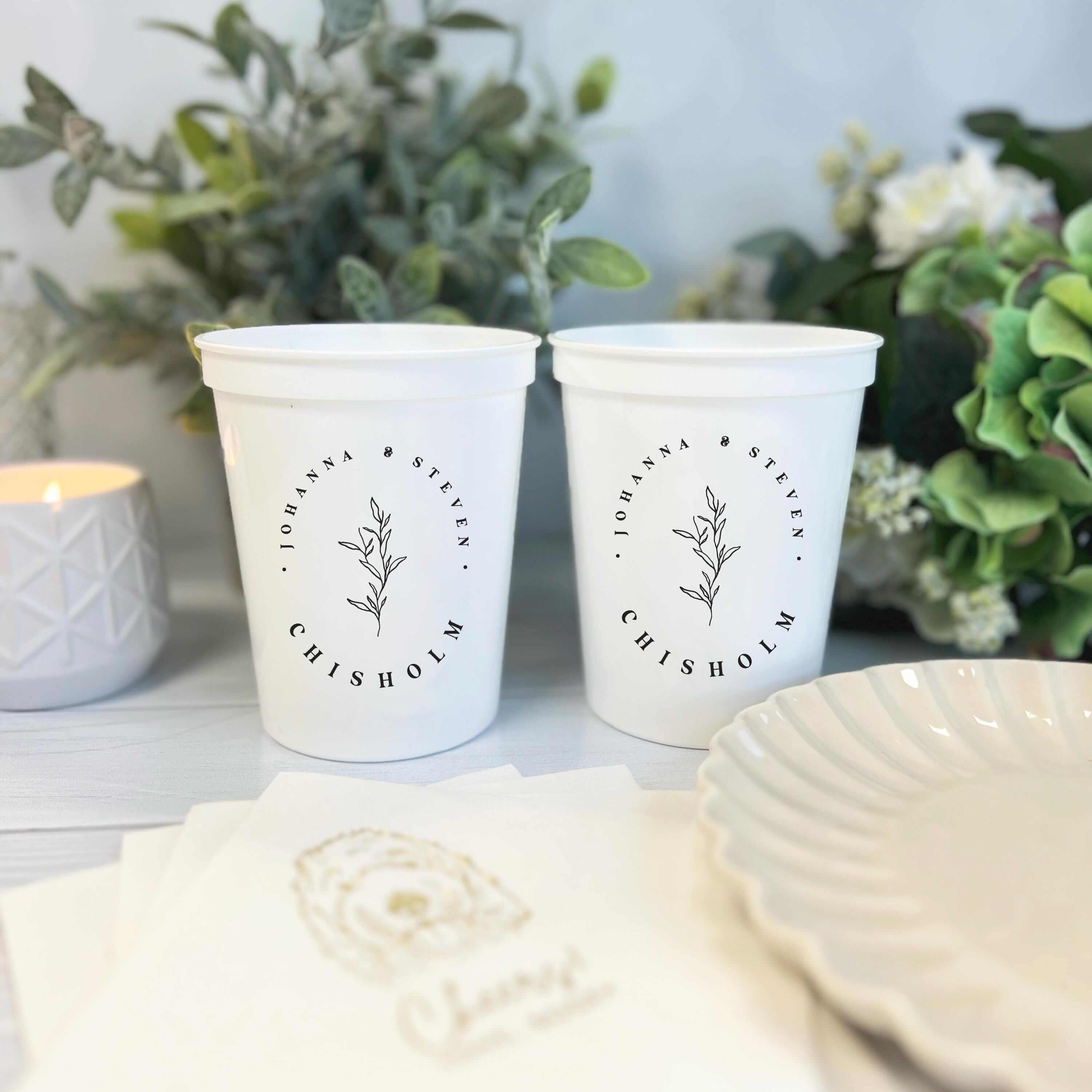 Two cream stadium cups with black botanical line art and "friends and family" text, displayed with greenery and wedding decor.