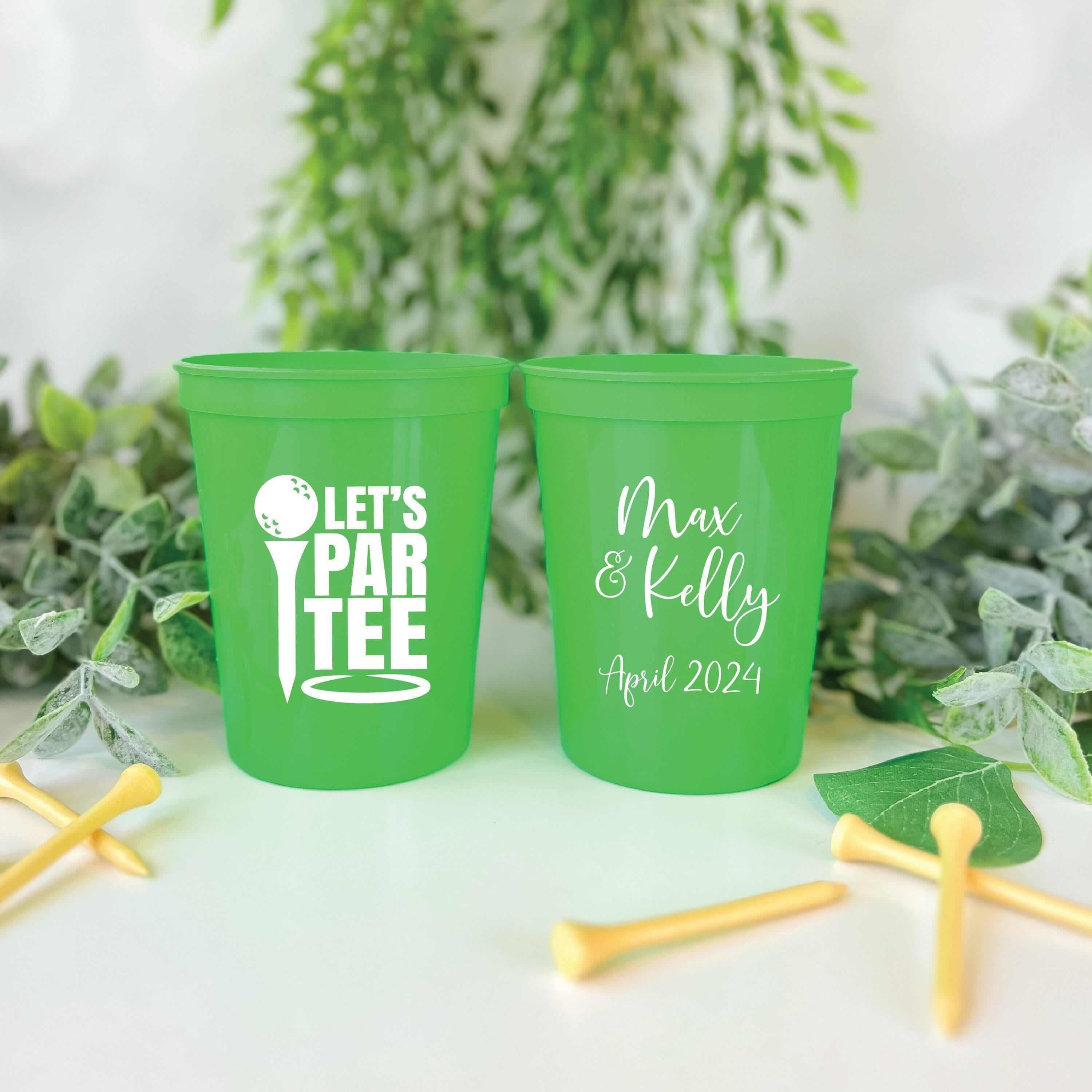 Bright green stadium cups with "Let's Par Tee" golf design and personalized names "Max & Kelly April 2024" surrounded by golf tees and greenery.