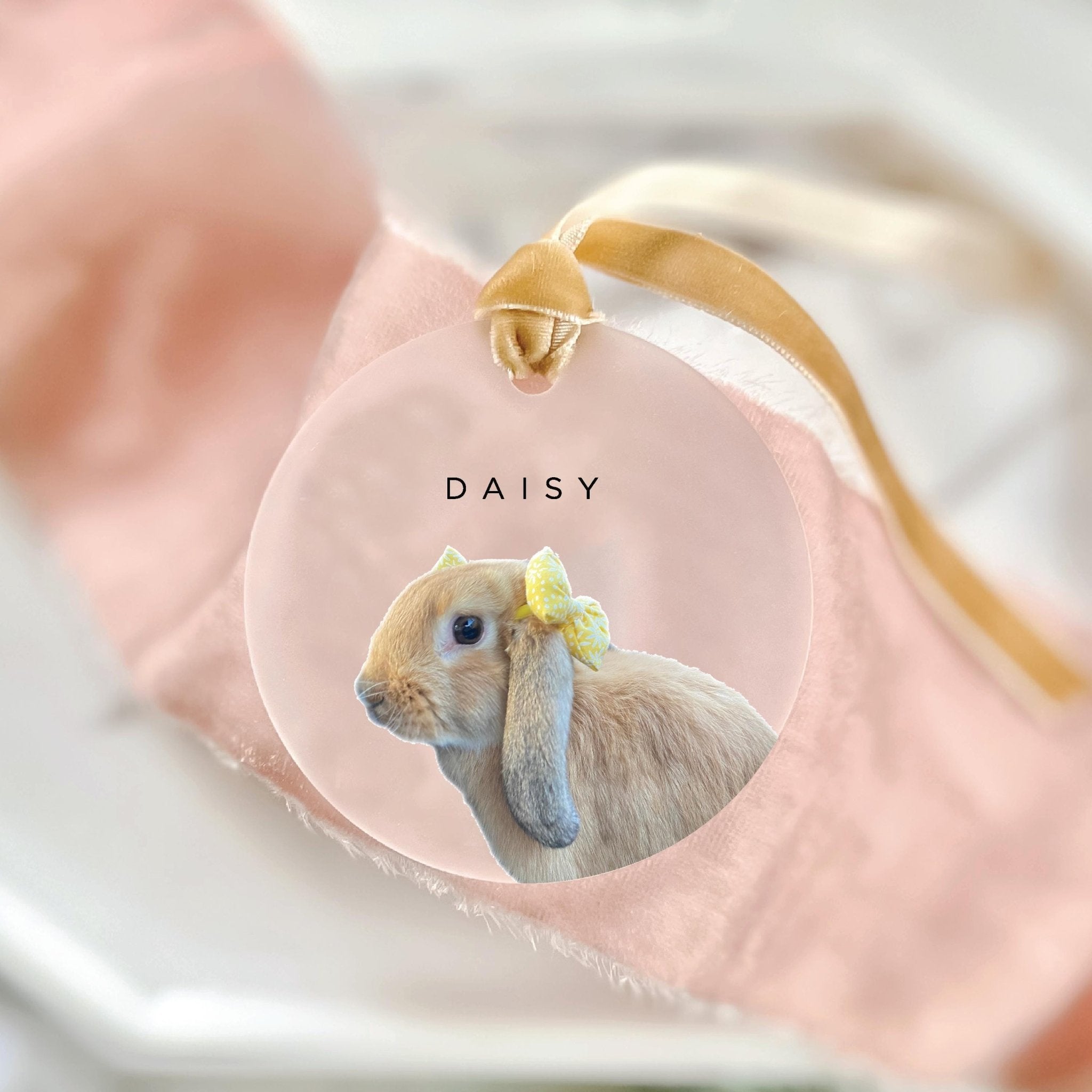 Frosted acrylic ornament with photo of gray rabbit wearing yellow flower crown, personalized with "DAISY" text, gold string attached