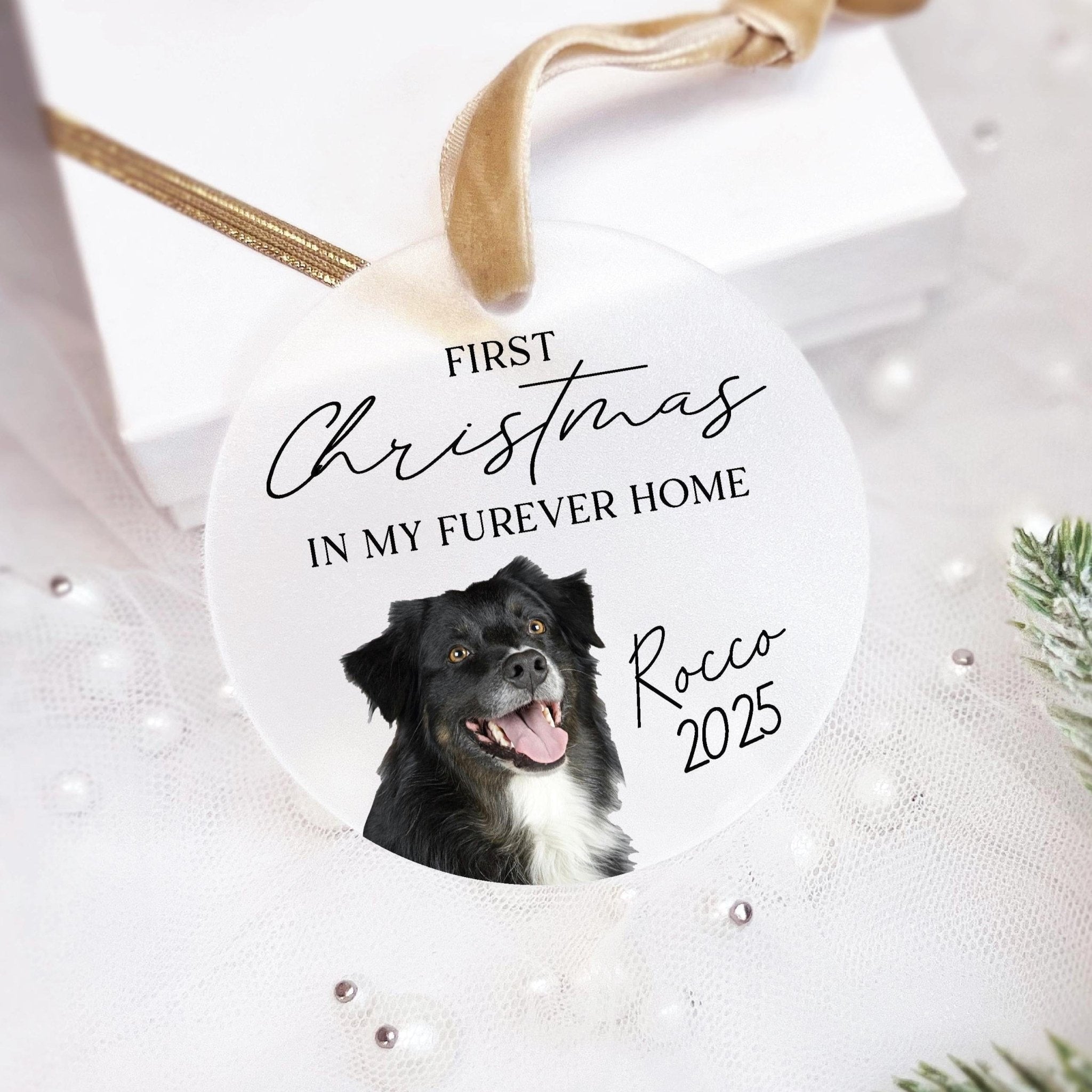 White acrylic ornament with gold ribbon featuring black dog photo, "First Christmas in My Furever Home" text, and "Rocco 2025" personalization.