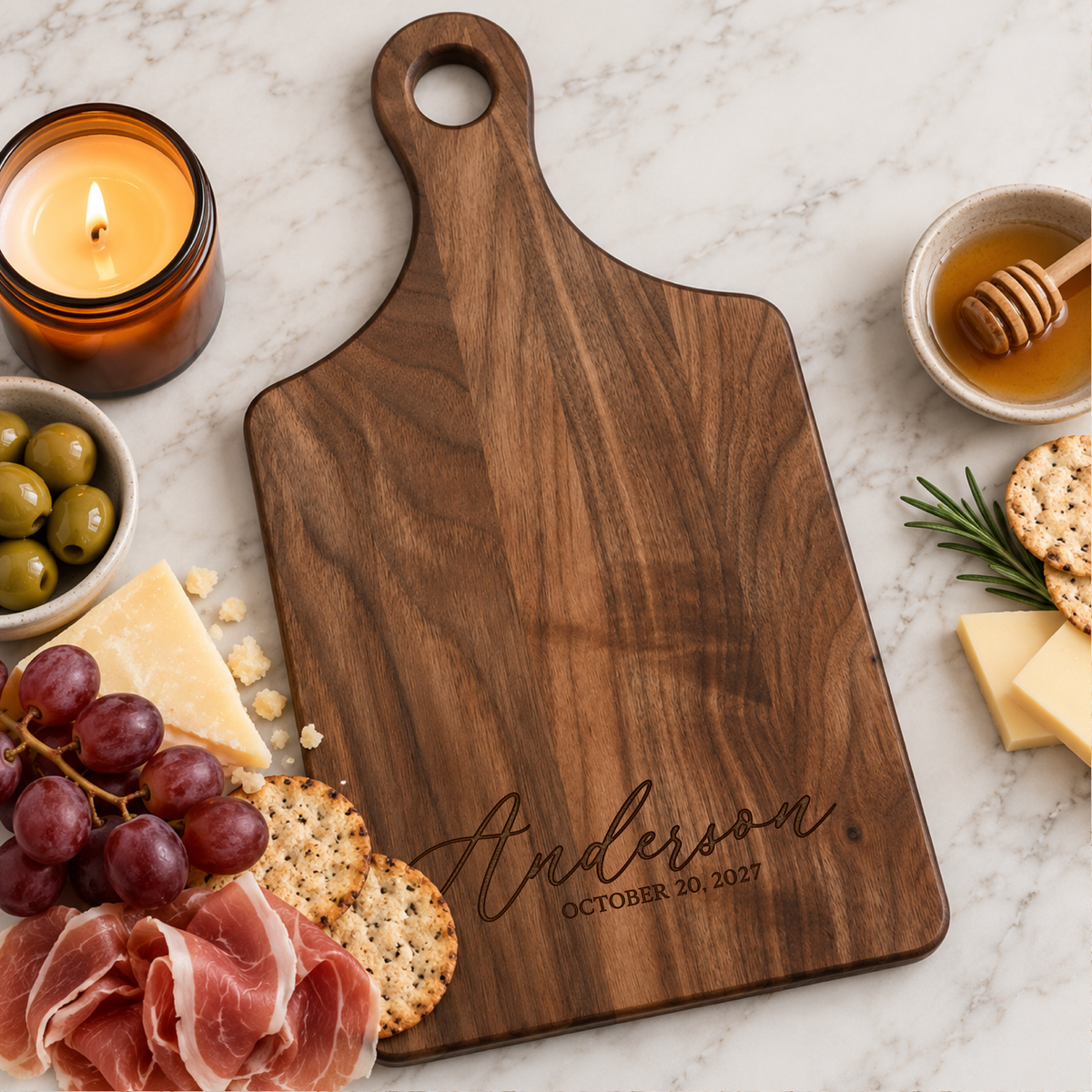 Custom engraved walnut charcuterie board personalized with Anderson and wedding date, surrounded by grapes, cheese, crackers, olives, and candle.