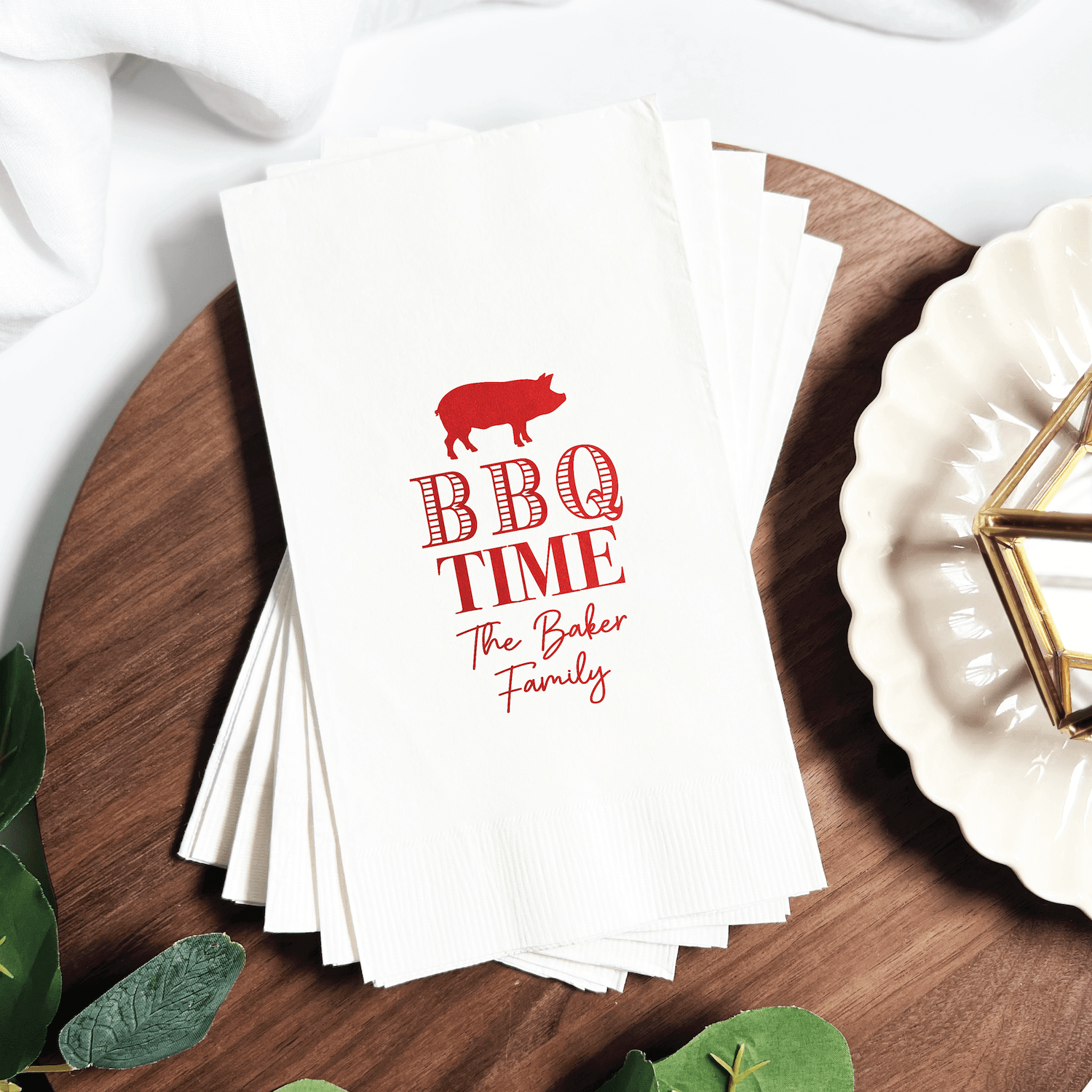 Stack of white napkins with red foil stamped BBQ pig design and "BBQ TIME The Baker Family" text