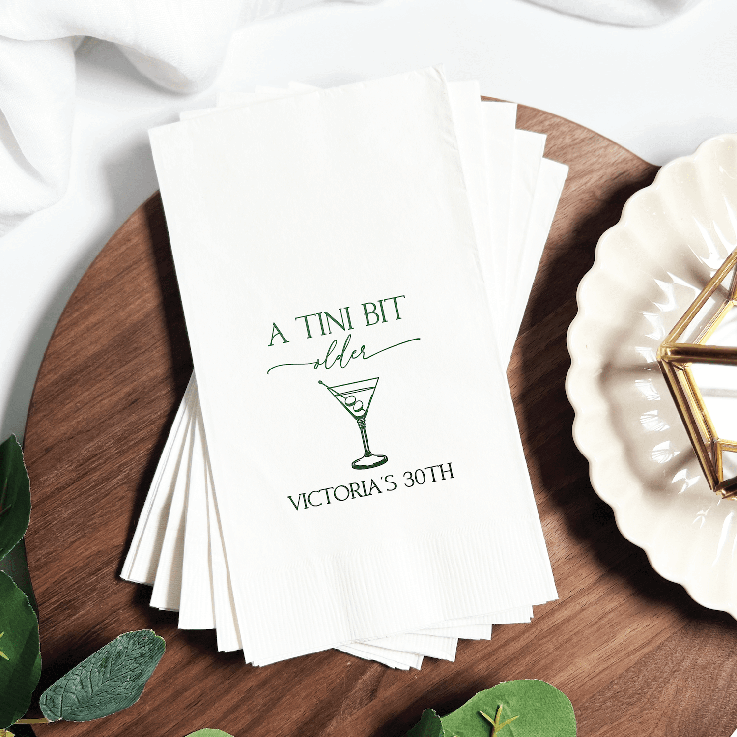 Stack of white napkins with "A Tini Bit Older" text and martini glass design, personalized with "Victoria's 30th" in green foil stamping.